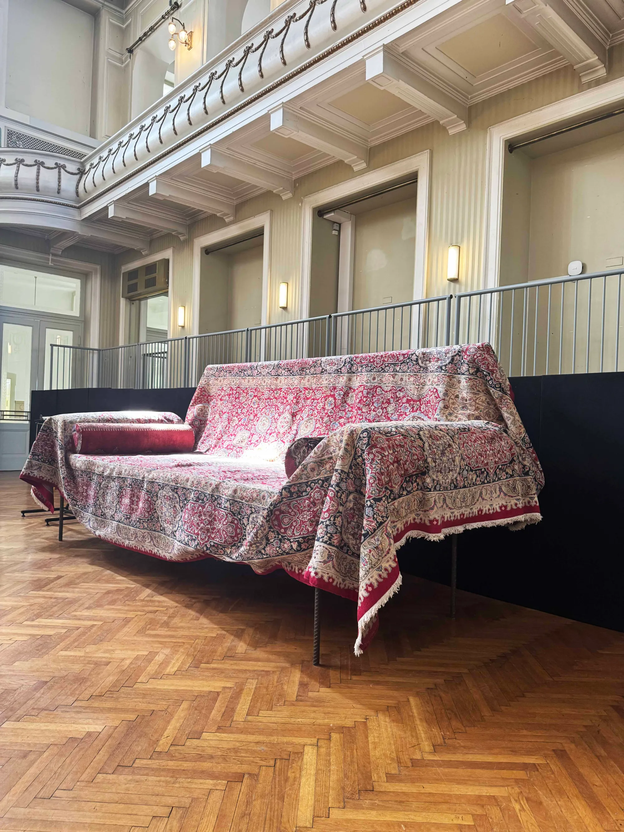 Parallel Vienna 2025: Installation by Gelitin in the Jugendstil Theater indoor sculpture garden, featuring an oversized sofa-like form draped with patterned carpets, blending humor and ornament.