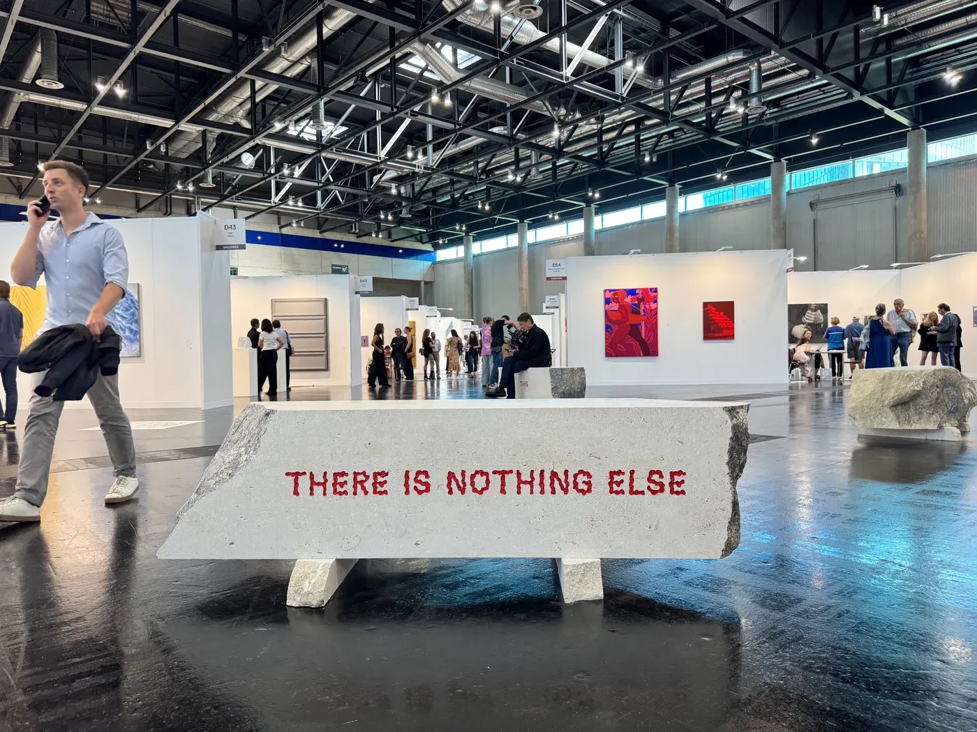 Stone bench with red text reading “THERE IS NOTHING ELSE” placed in the hall of Vienna Contemporary 2025 at Messe Wien, with booths and visitors in the background.