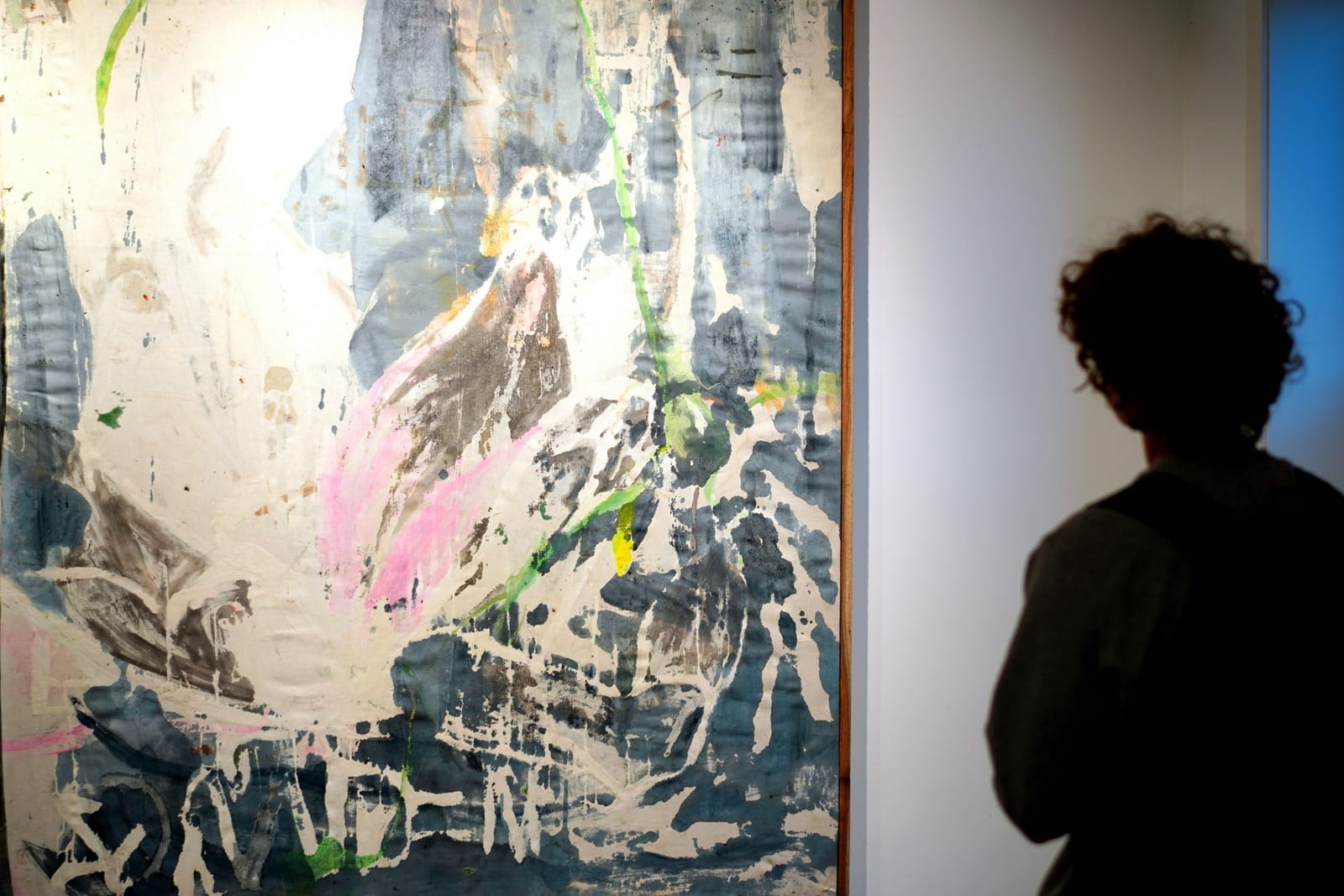 Ruth Devriendt’s 2025 acrylic painting Gonesick, shown on a gallery wall with a viewer standing nearby. Large expressive brushwork in soft and dark tones. Photo by John Devos.