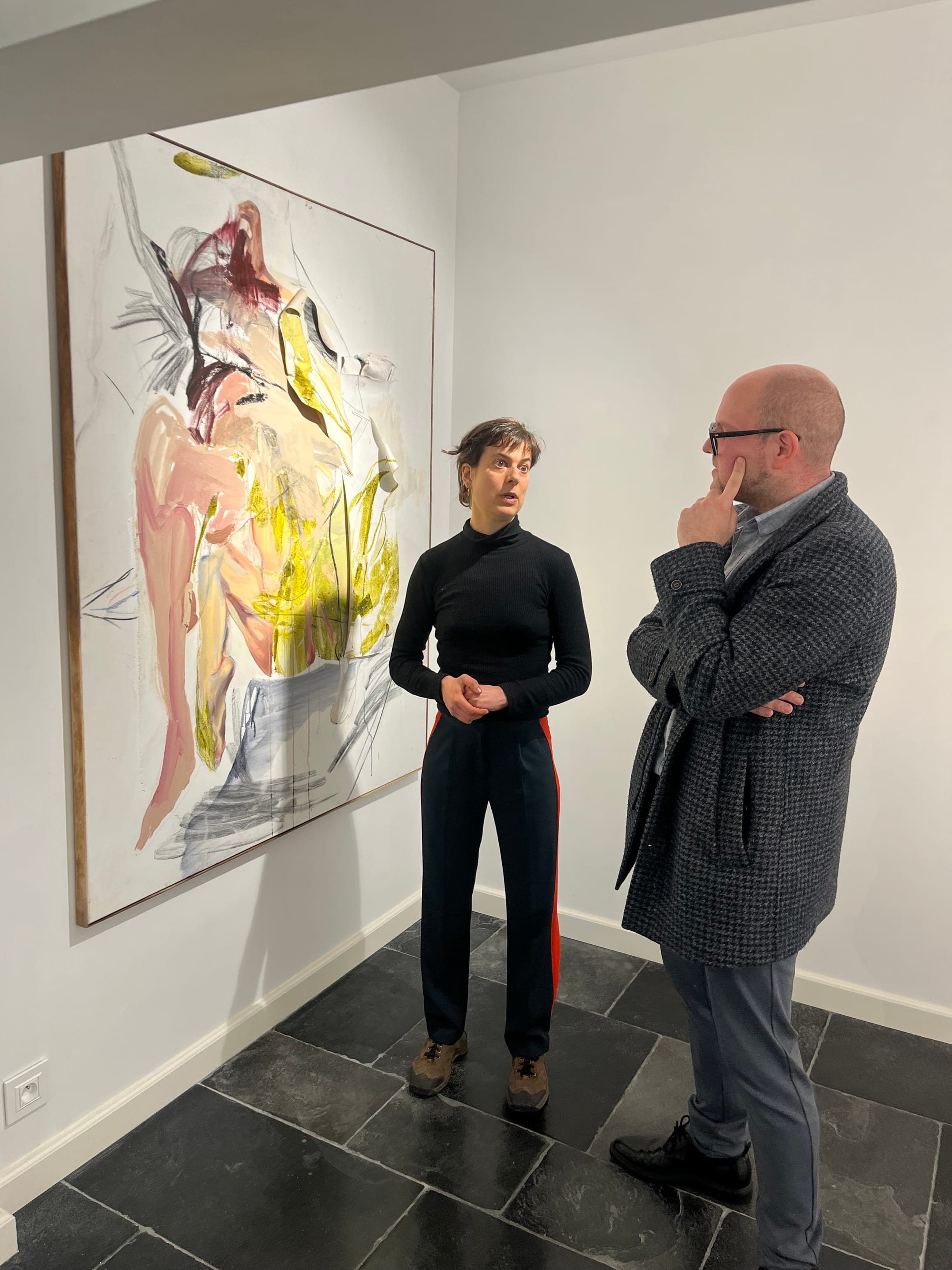Two people standing in front of a large abstract painting during a conversation at Black Swan Gallery, captured on the gallery floor with stone tiles and white walls