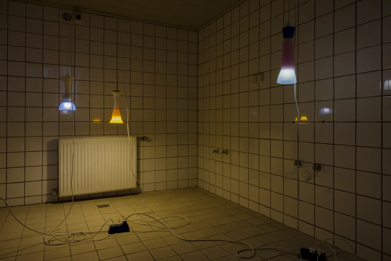 Installation by Lazar Lyutakov in a tiled room at Kunstverein Schattendorf, showing cables, power strips and a radiator arranged on the floor.