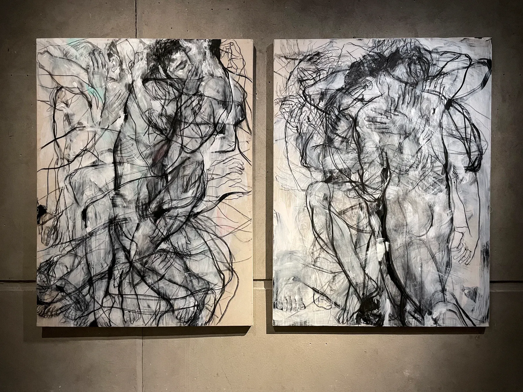 Two large expressive black-and-white figurative paintings by Maria Naidyonova, each showing layered gestural bodies in motion, displayed side by side in a gallery setting.