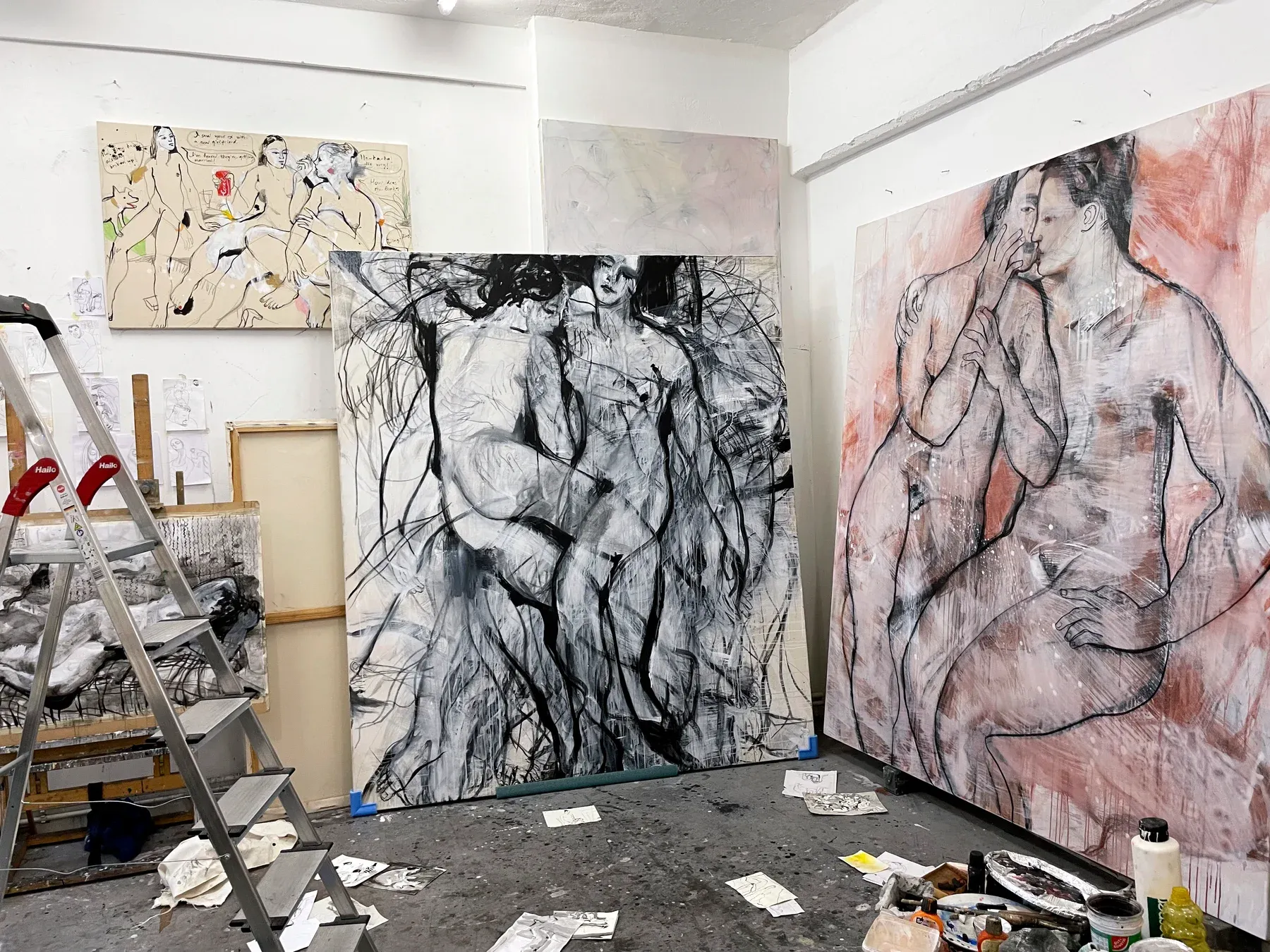 A studio interior with large figurative canvases by Maria Naidyonova placed around the room, alongside sketches, tools, and a ladder.