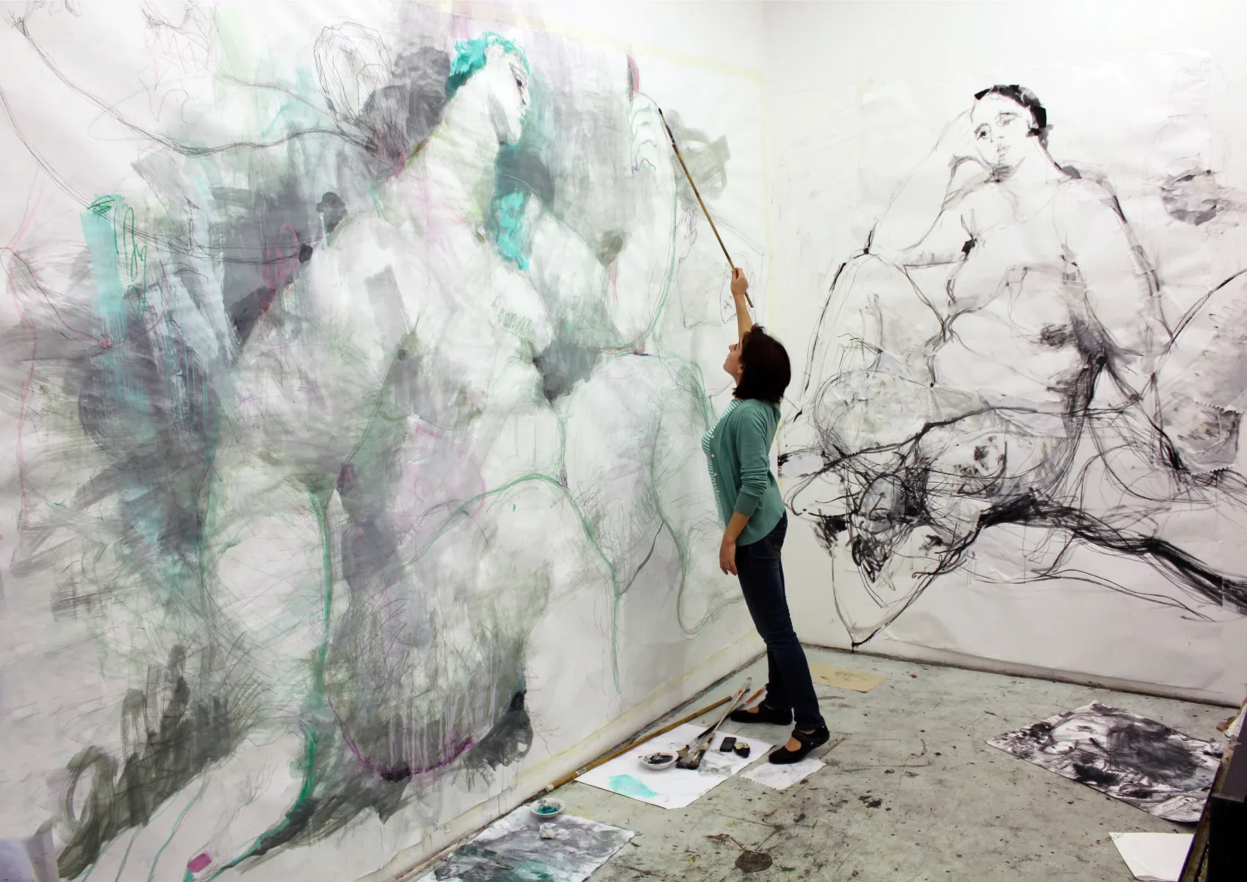Maria Naidyonova working in her studio on a large graphite and mixed-media wall drawing depicting monumental intertwined figures.