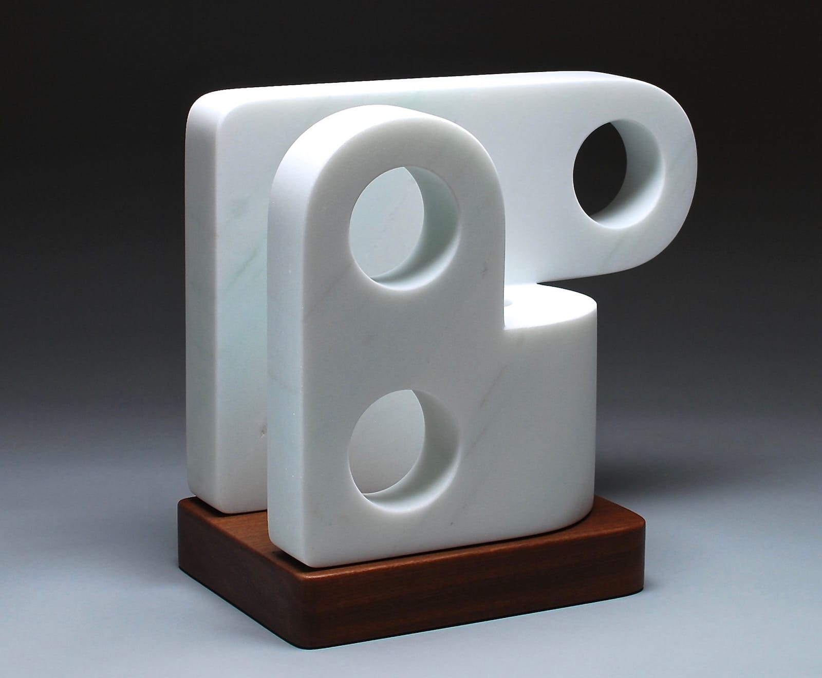 Marble sculpture by Chris Cassimatis titled Part# 002, featuring interlocking white geometric forms with circular cutouts on a wooden base. Image Courtesy of the Artist