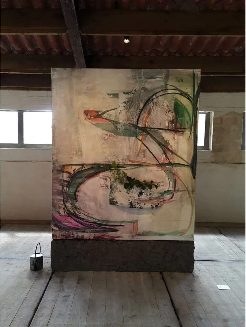 Outdoor installation by Ruth Devriendt from the series Paintings in flux, a large painted canvas mounted on a wooden base inside a barn-like space with natural light. Image courtesy of the artist.