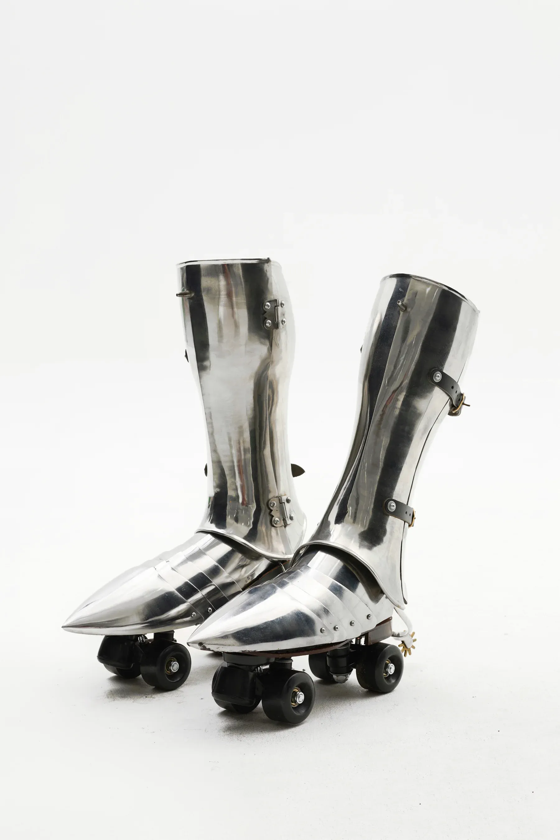 Pair of sculptural metal boots mounted on roller skate wheels, photographed against a white background.