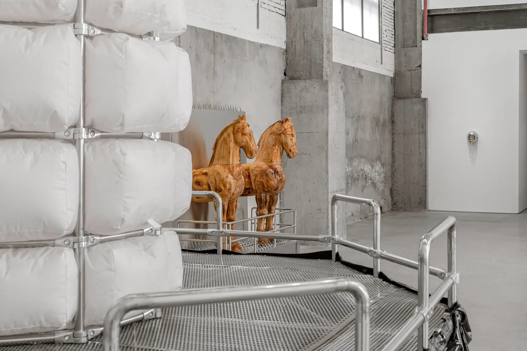 Gene Gallery, Shanghai, Installation view ( artist Xiaozhou Liao) showing a tall padded tower structure beside two wooden horse sculptures positioned in front of a reflective metal panel.