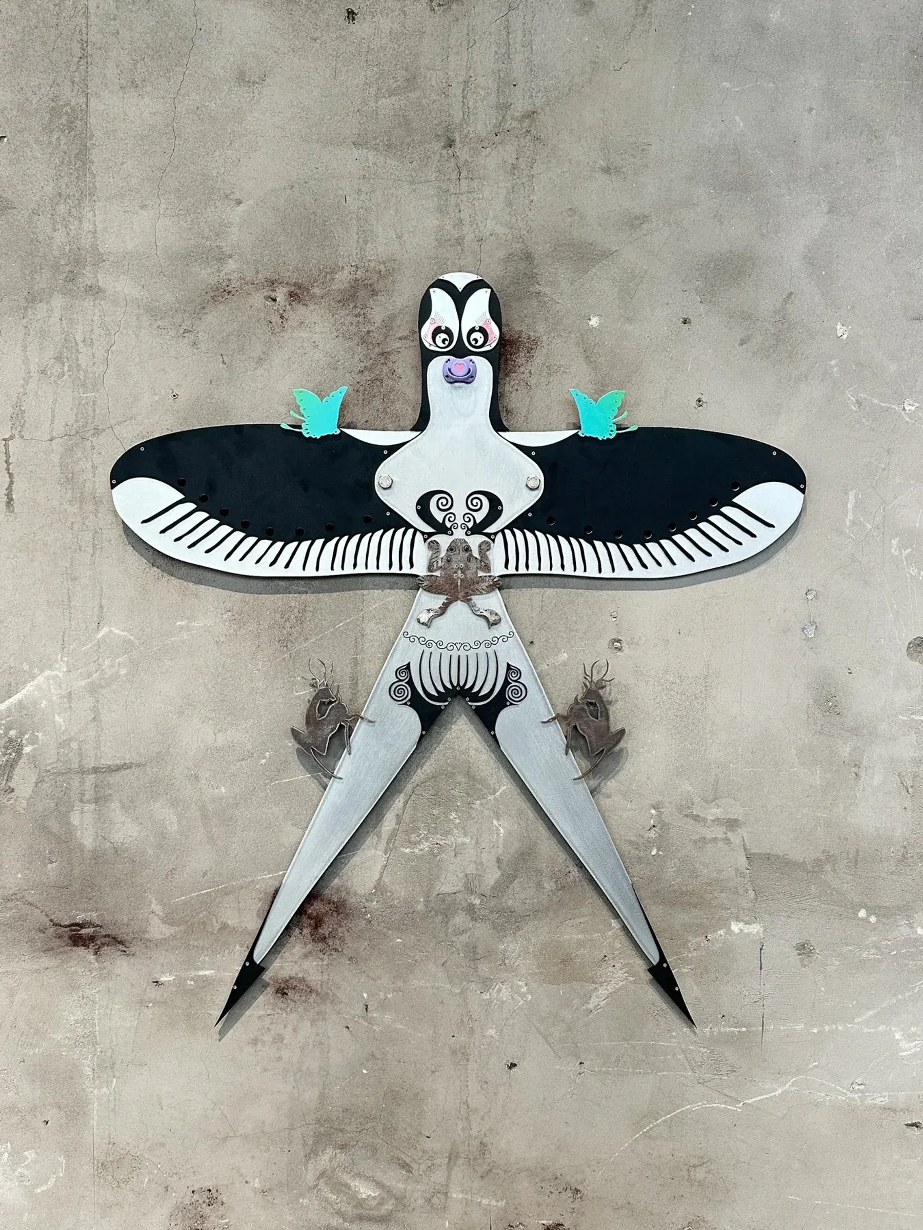 Wall mounted sculpture titled Yuan, featuring a stylized bird figure installed against a weathered concrete surface.