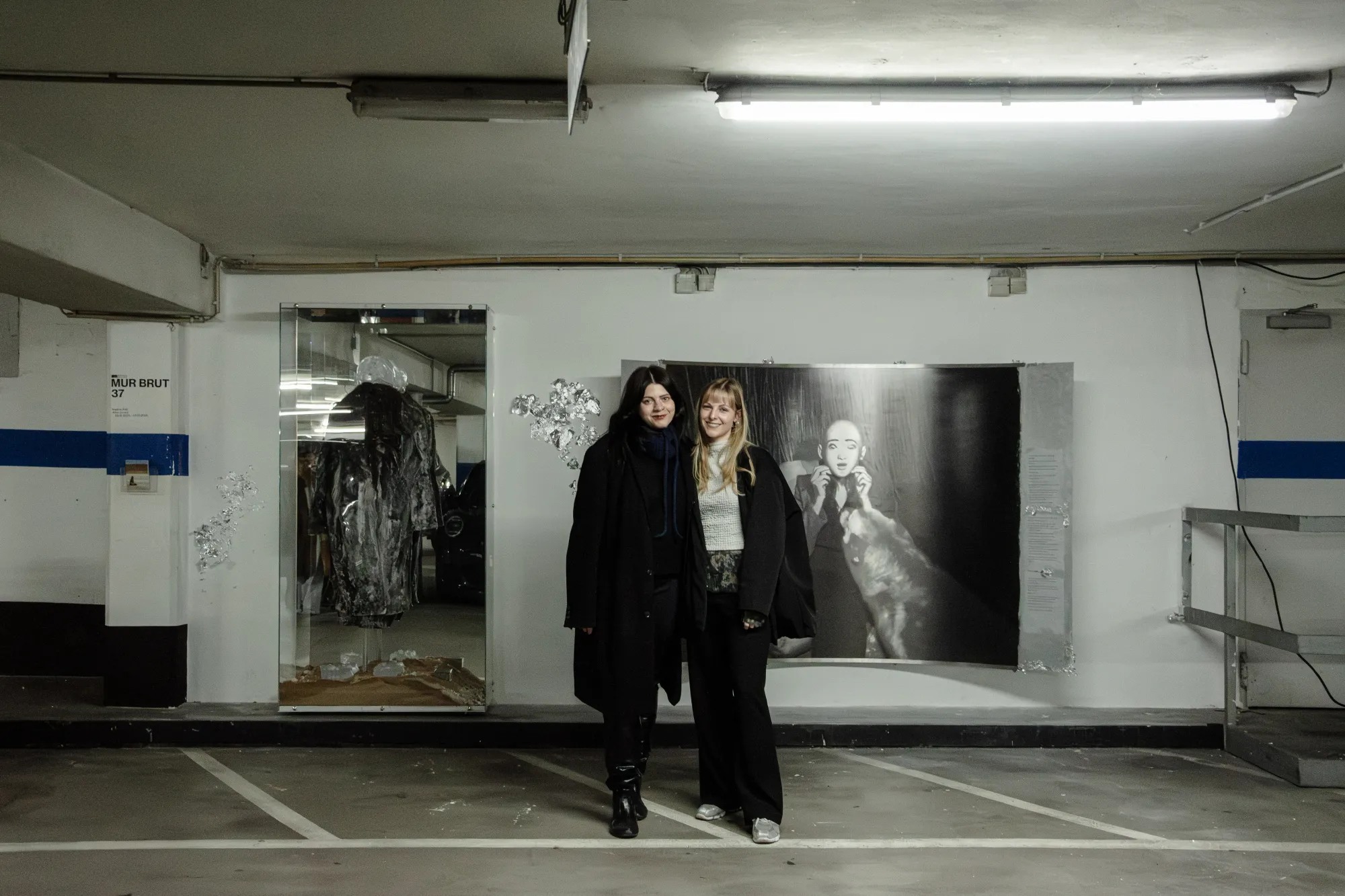 Installation view of After Unrast by Nadine Karl at Kunsthalle Düsseldorf, showing the artist on the left, standing in front of the installation with sculptural and photographic works visible in the background.