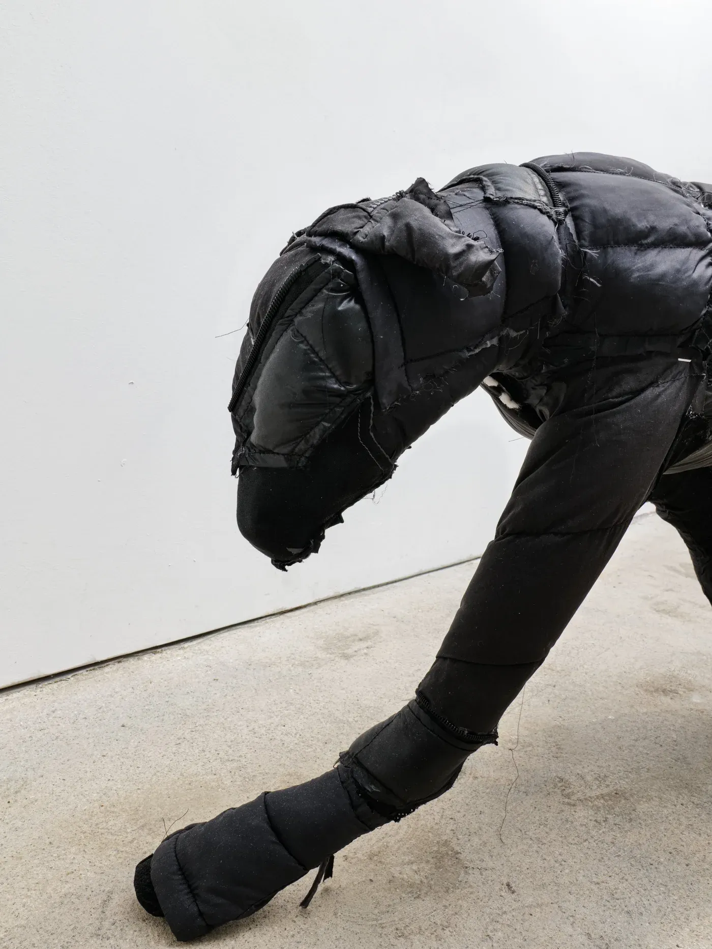 Close up of a black dog like sculpture made from stitched puffer jacket fabric and foam, leaning forward on extended front legs.