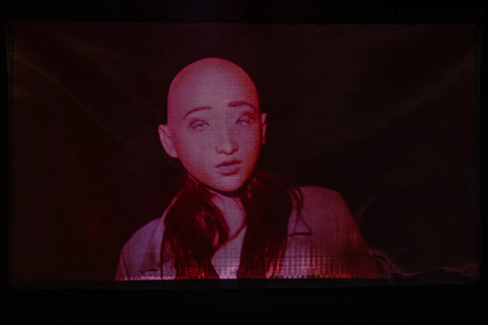 Installation detail from Epiphenomenon by Nadine Karl, showing a projected image of a human figure in red tones within a darkened space.
