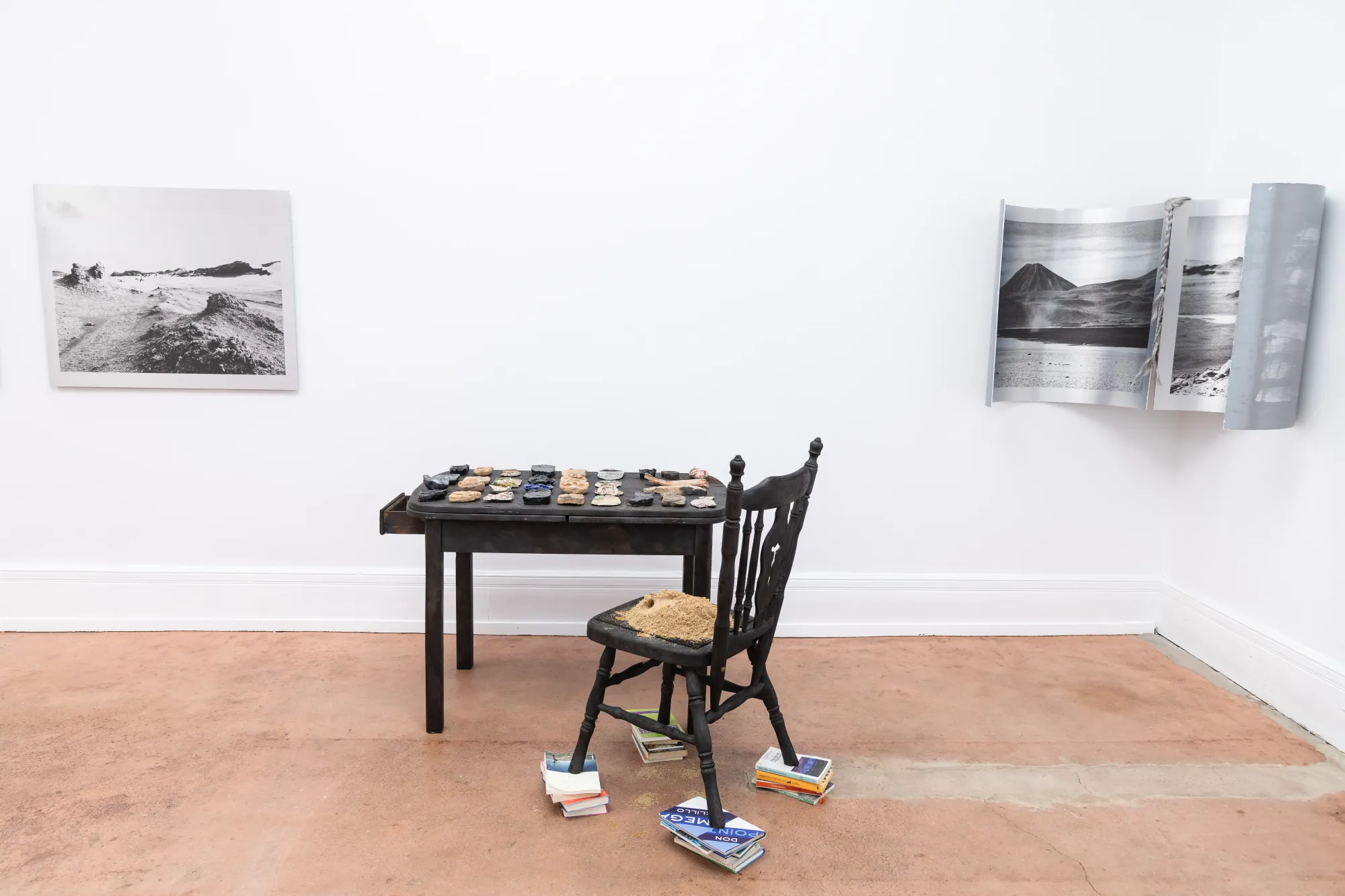 Installation view of Nadine Karl work Epiphenomenon, showing a table with sculptural elements, a chair, and photographic works mounted on white gallery walls.