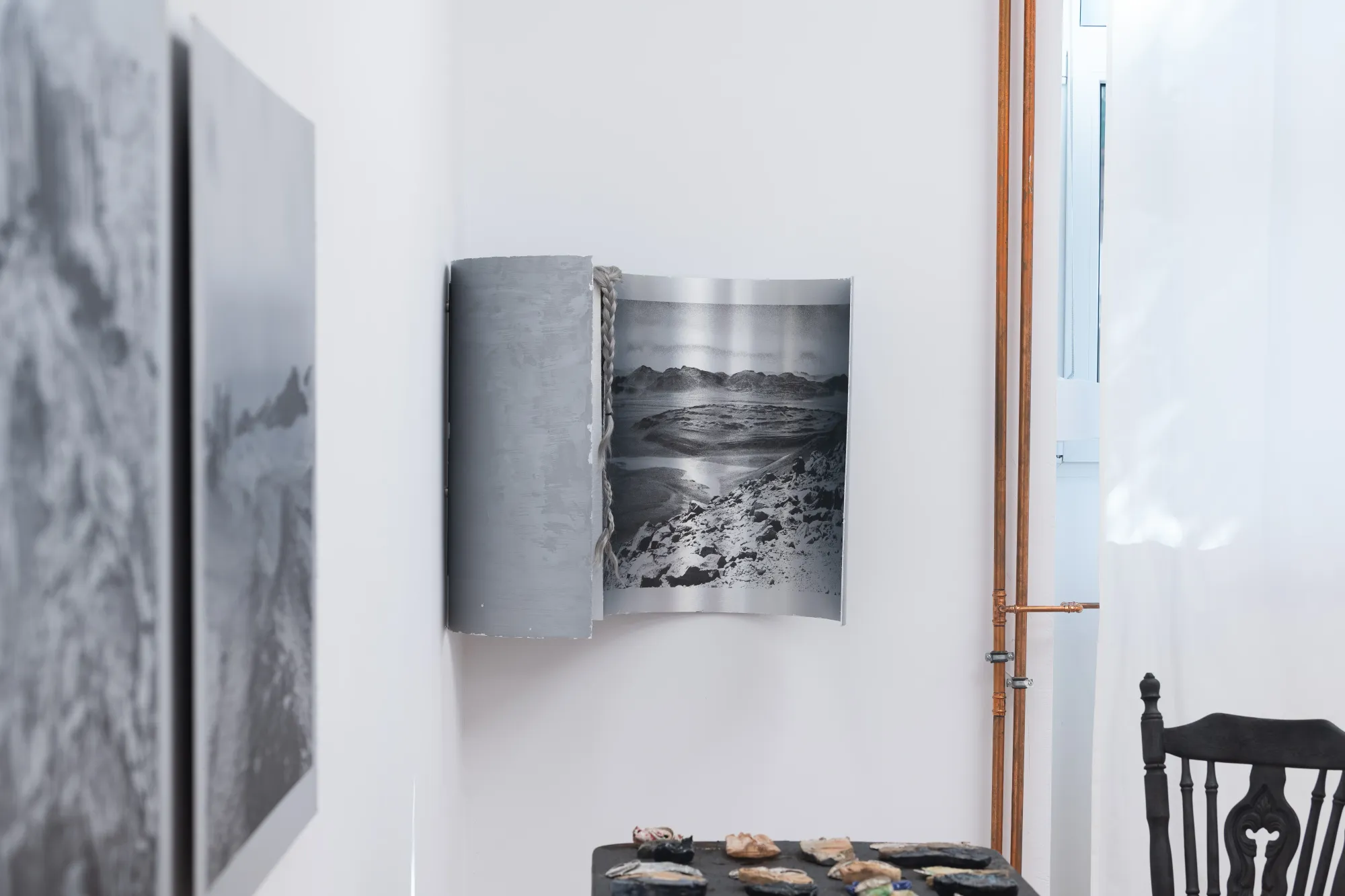 Side view of Epiphenomenon by Nadine Karl, showing curved photographic panels, a table with sculptural objects, and part of the gallery architecture.