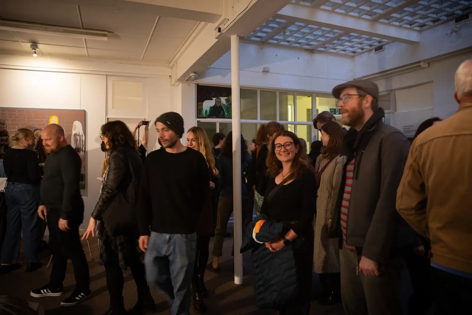 Gallery visitors walking through Paes’ exhibition with multiple figurative paintings installed across white walls.