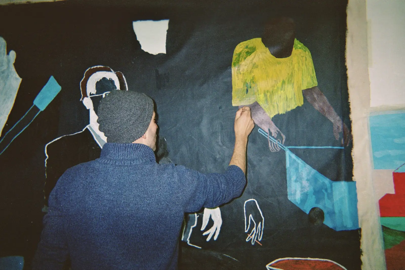 Paes, artist,  painting a large black canvas with figurative elements in his studio.