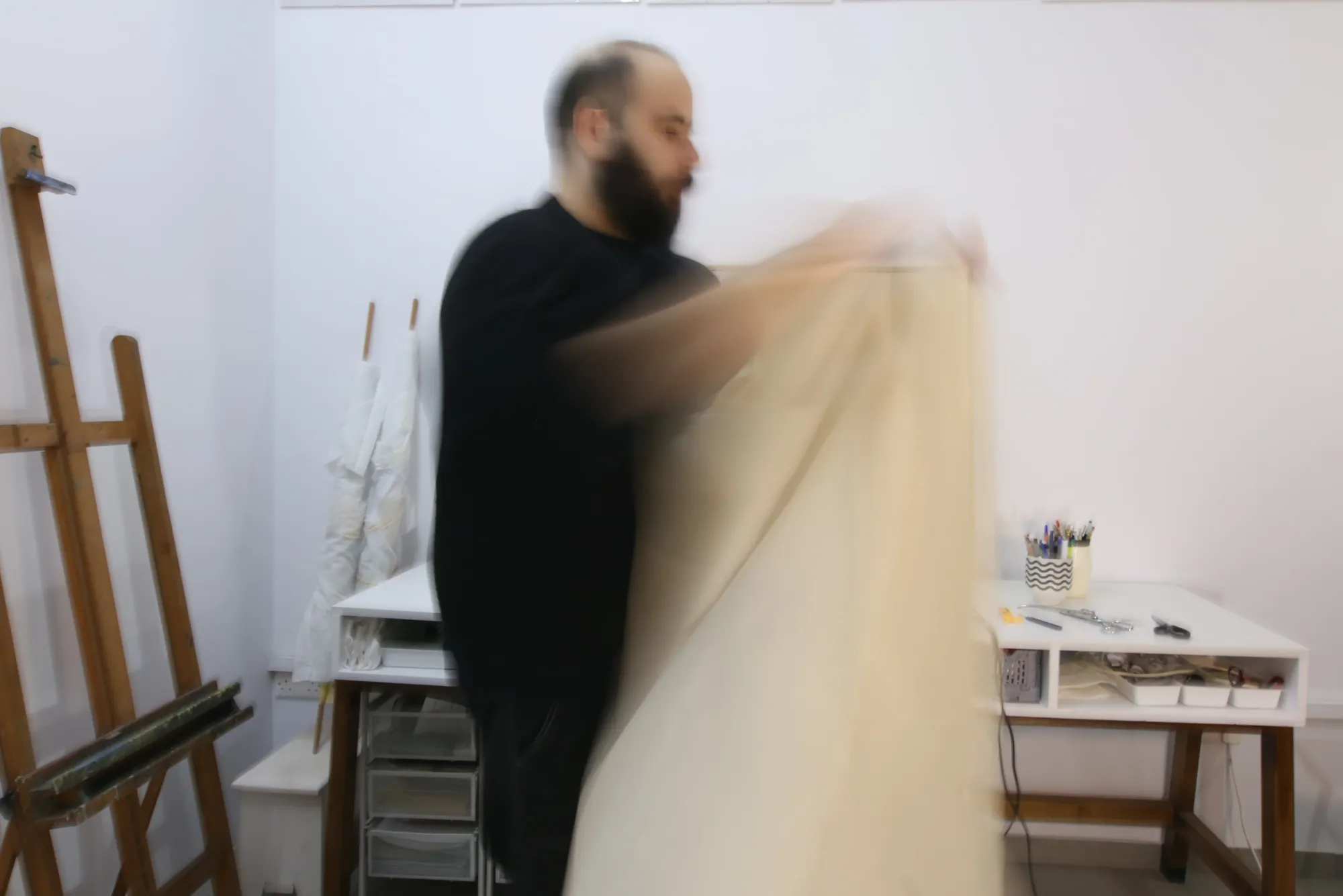 Avraam Hirodontis in his studio handling raw canvas fabric, the motion slightly blurred as material is lifted and folded during the making process.