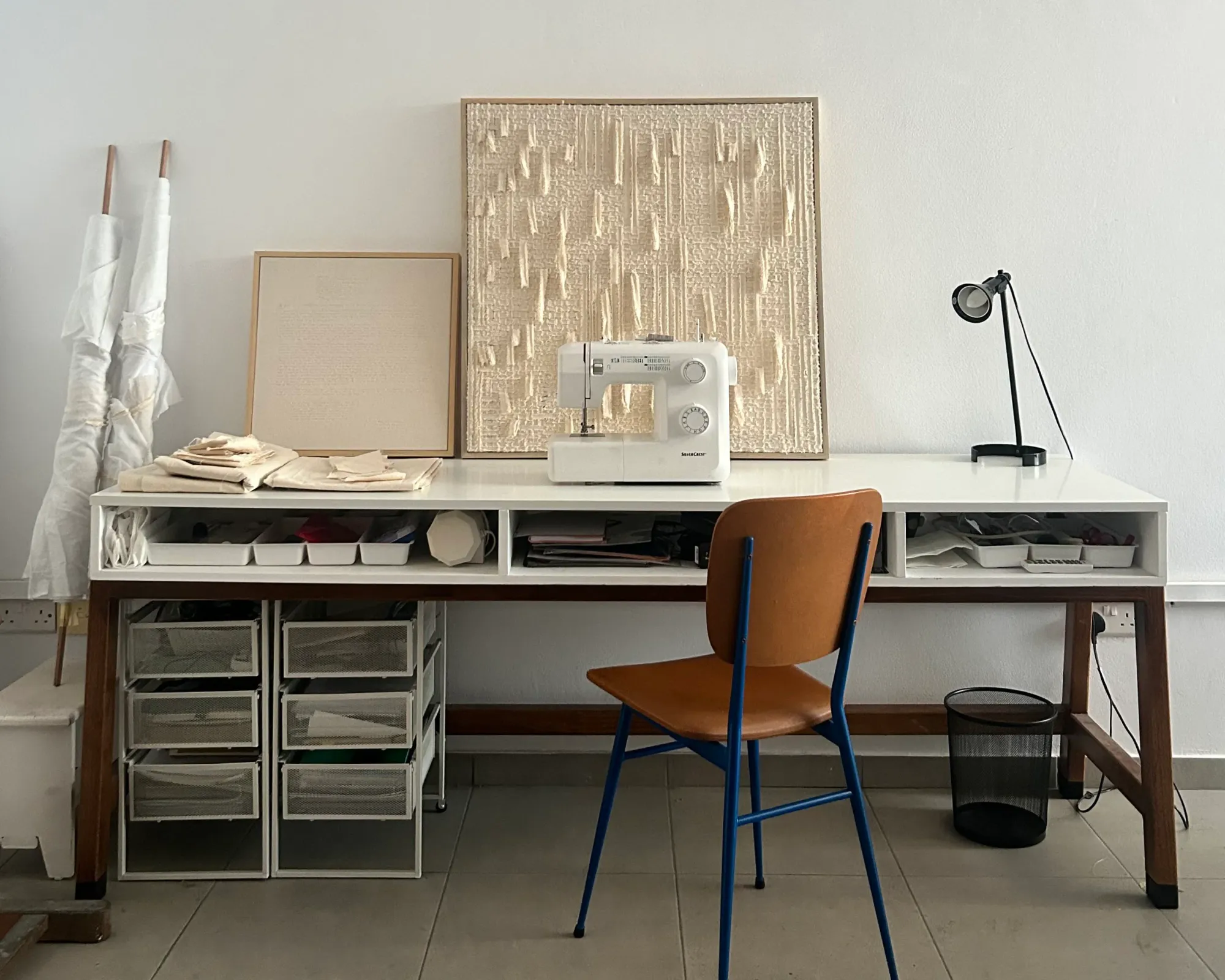 Avraam Hirodontis’ studio workspace with sewing machine, folded canvas, tools, and a finished textile work resting against the wall.