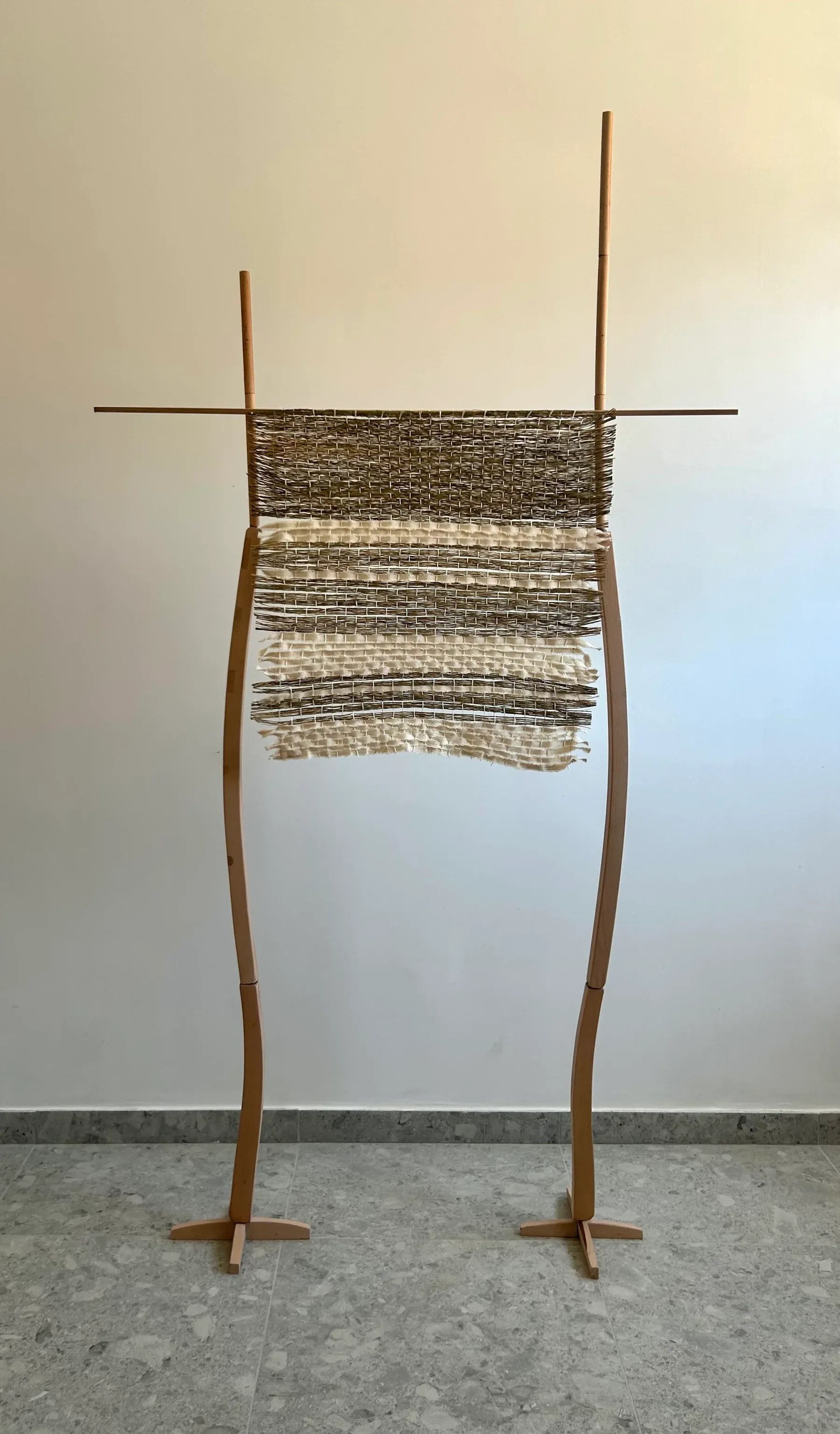 A freestanding woven structure made of wood, straw and canvas fabric with layered weaving shifting between tight and open areas.