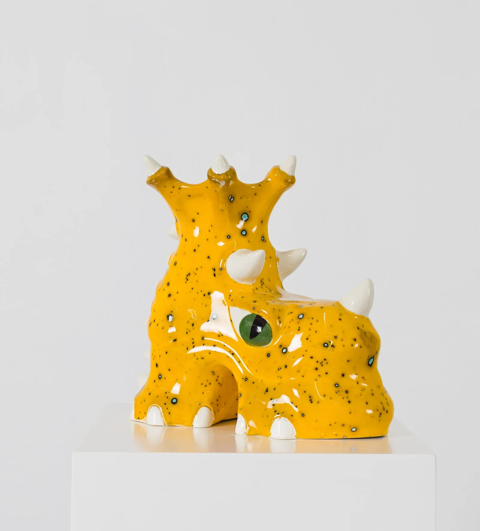 Yellow ceramic sculpture with horn-like forms and speckled surface, presented on a white pedestal.