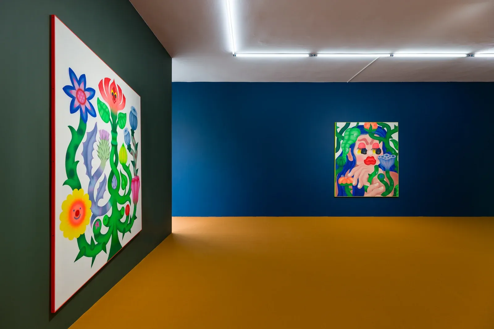 Wide installation view of a gallery space with brightly colored figurative paintings installed on deep blue walls and a contrasting floor.