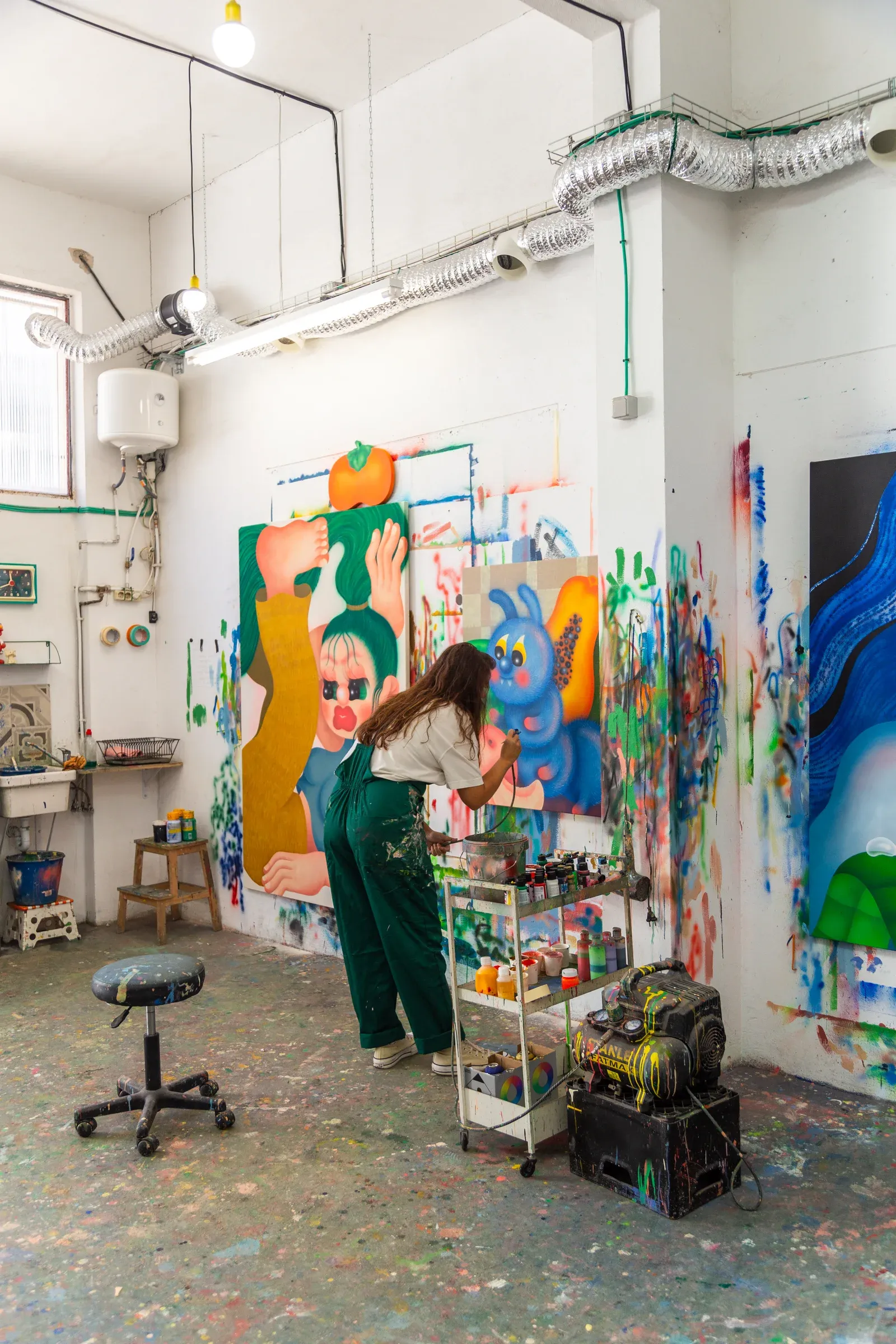 Fátima de Juan, Artist painting a large-scale figurative work in her studio, surrounded by paint marks, tools, and works in progress.