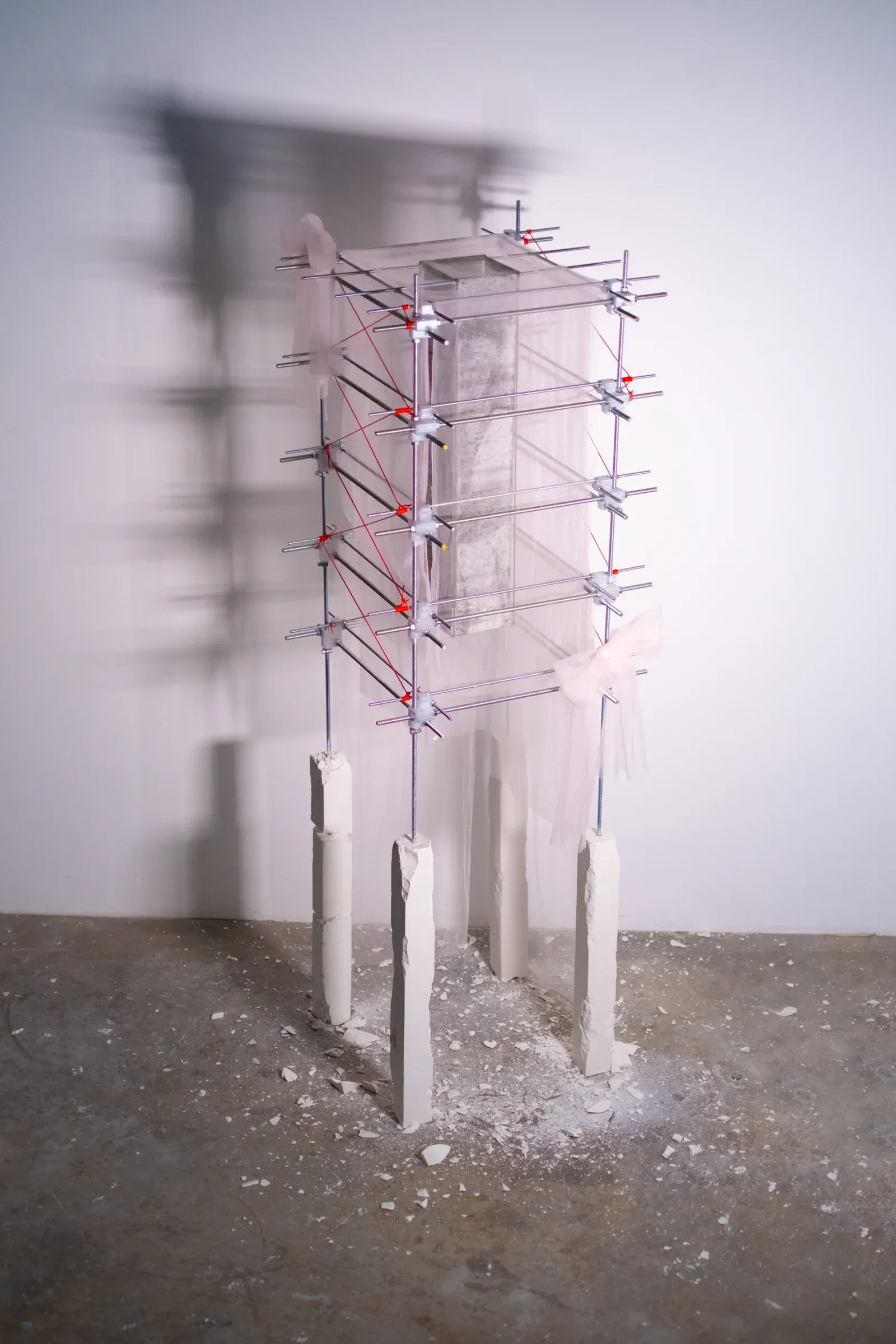 Alexander Kaye, Self-Portrait II, 2025, steel and mesh fabric structure with plaster columns and charcoal drawing suspended within a compressed grid framework.