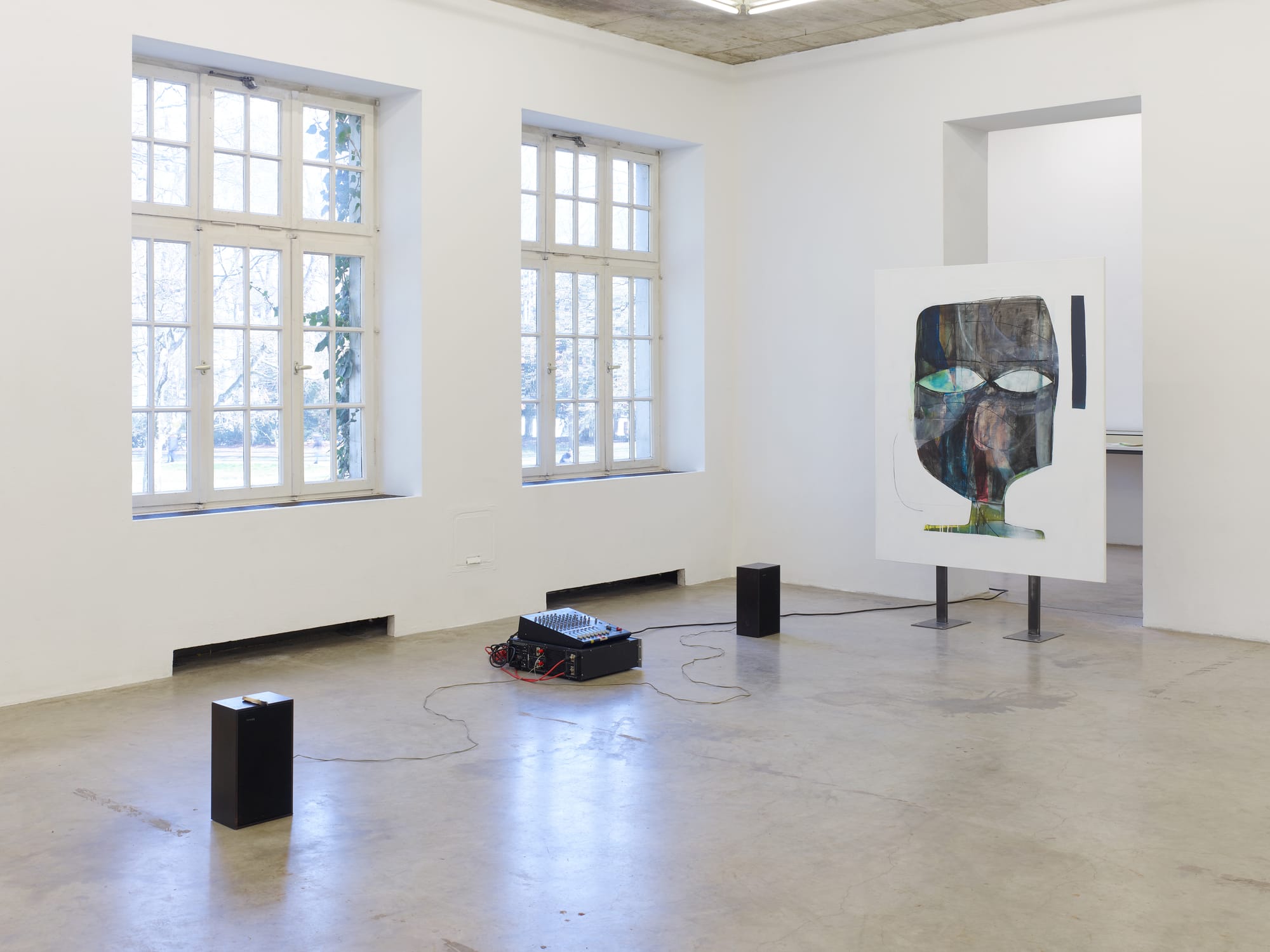 Installation view of Tom Król’s exhibition at Neuer Aachener Kunstverein featuring a large figurative painting on freestanding supports and audio equipment placed on the gallery floor
