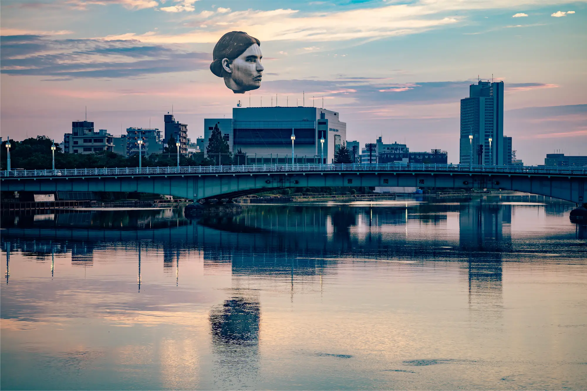 目 [mé] art collective, artwork -  masayume (2019–2021) floating head sculpture suspended above a river and bridge in Tokyo at sunset during Tokyo Tokyo FESTIVAL Special13.