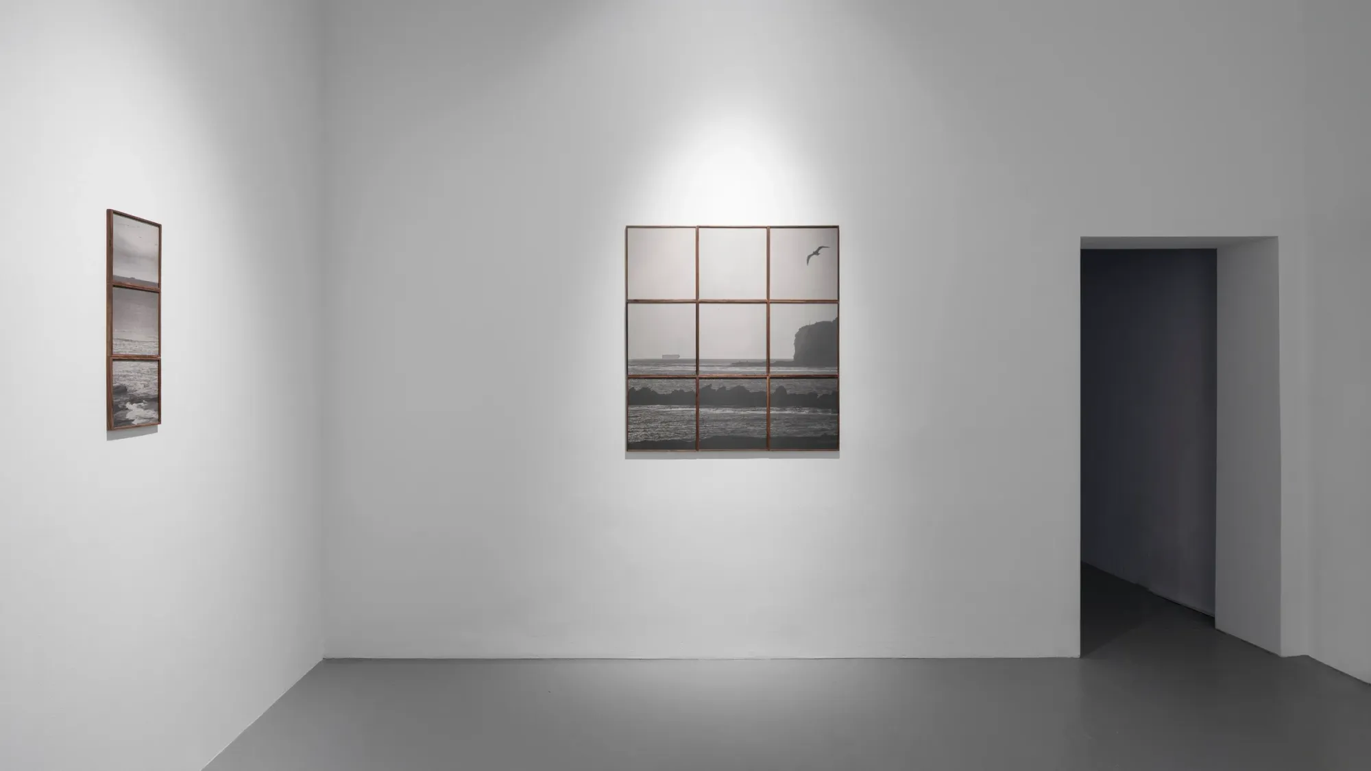 Grid-based photographic work showing coastal landscape divided into square sections, accompanied by vertical series of framed images on adjacent wall, sparse white gallery interior, Kaya & Blank Intermodal basis Frankfurt