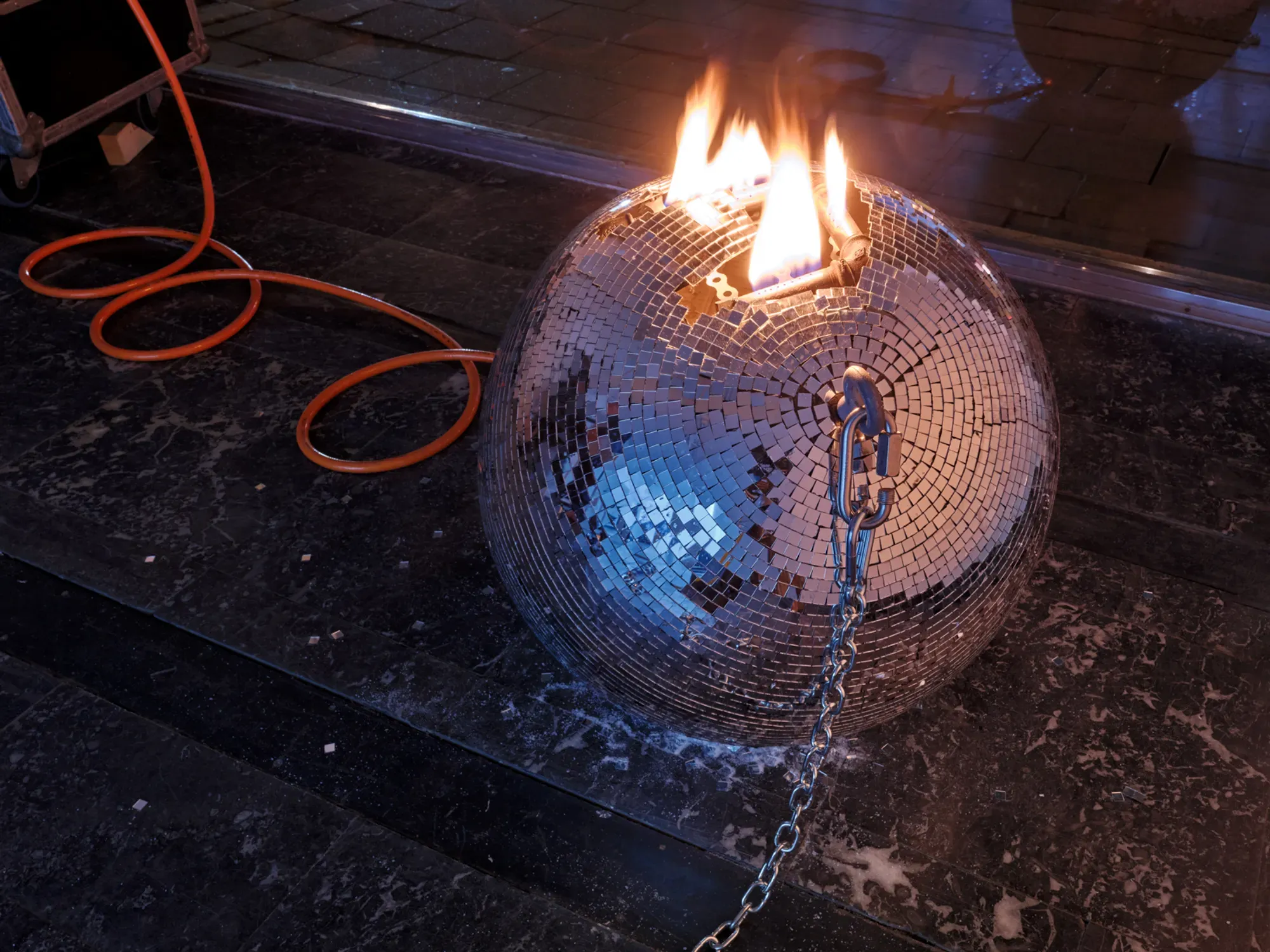 Detail view of Banks Violette’s Untitled (Discoball), 2026, showing a mirrored sphere ignited with flame and attached to a metal chain inside the gallery space.