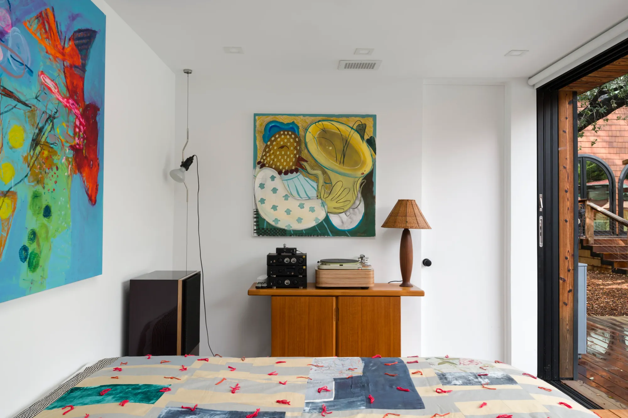 Installation view of Dinner Table at Simchowitz Hilltop, Los Angeles, featuring paintings by Andrey Samarin and Lera Derkach displayed in a staged bedroom interior with bed, record player and wooden deck outside.
