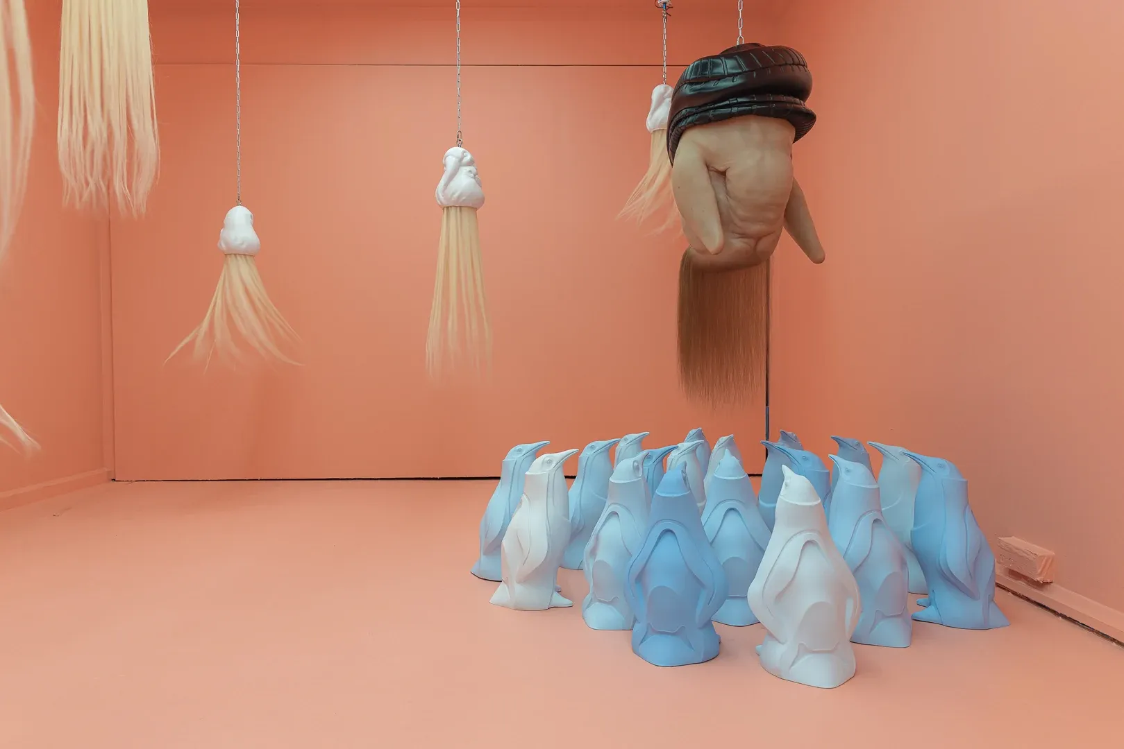 Passage gallery Sydney current Suspended hybrid figure sculpture by Patricia Piccinini above a cluster of blue penguin forms in pink exhibition 