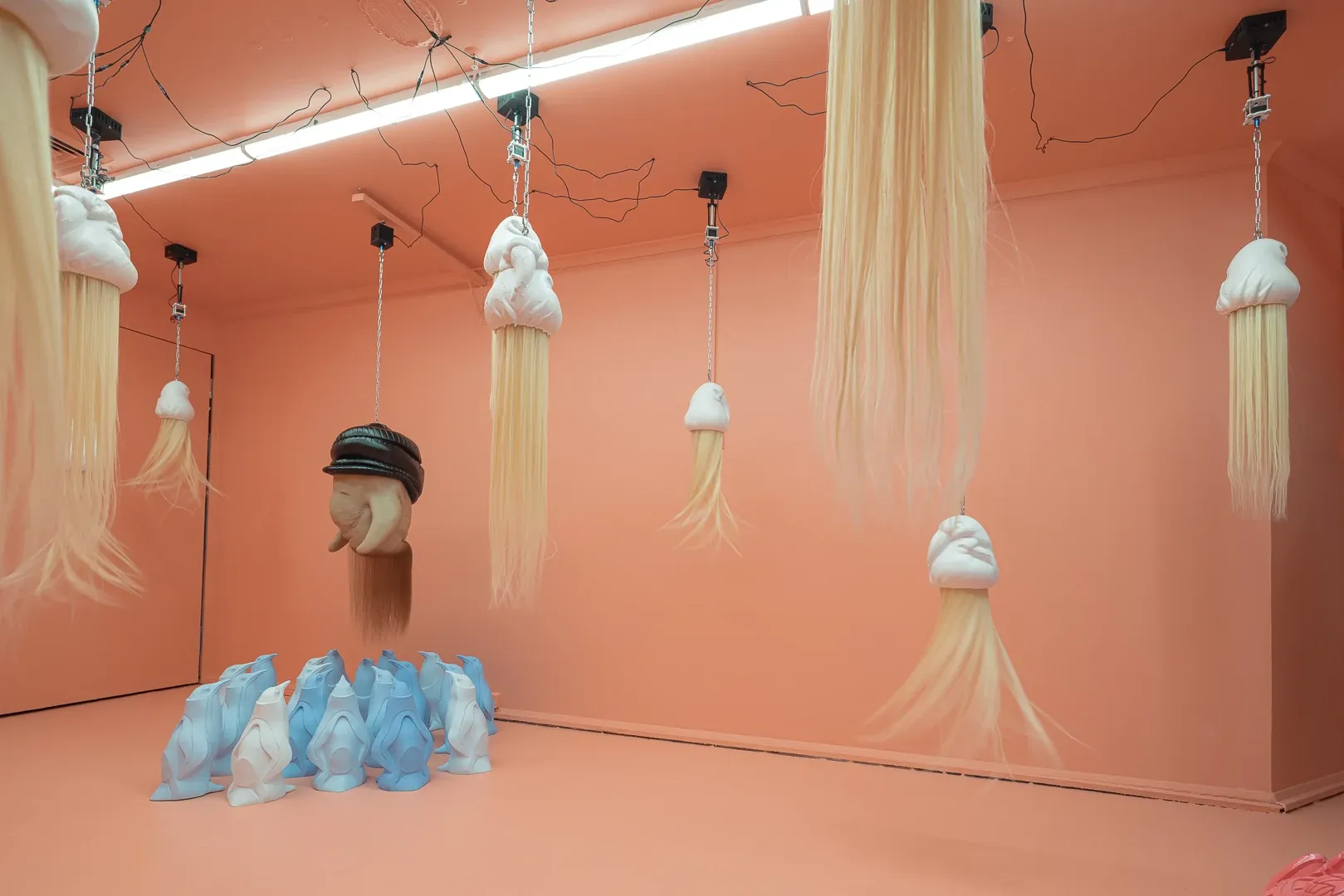 Installation view of Patricia Piccinini at Passage Gallery Sydney with hanging kinetic hair sculptures and penguin group in pink exhibition space