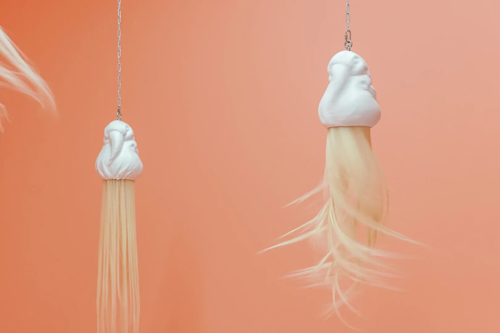 Detail of hanging kinetic sculpture by Patricia Piccinini with long synthetic hair strands moving in exhibition space