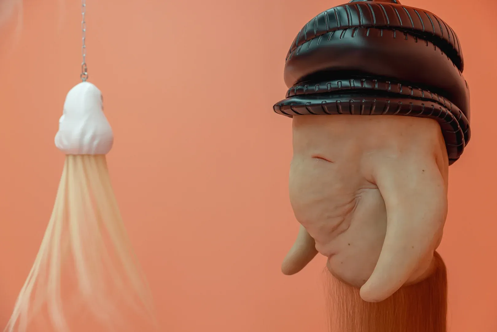 Close up of hybrid sculptural head by Patricia Piccinini with fleshy surface and black crown element suspended in exhibition space