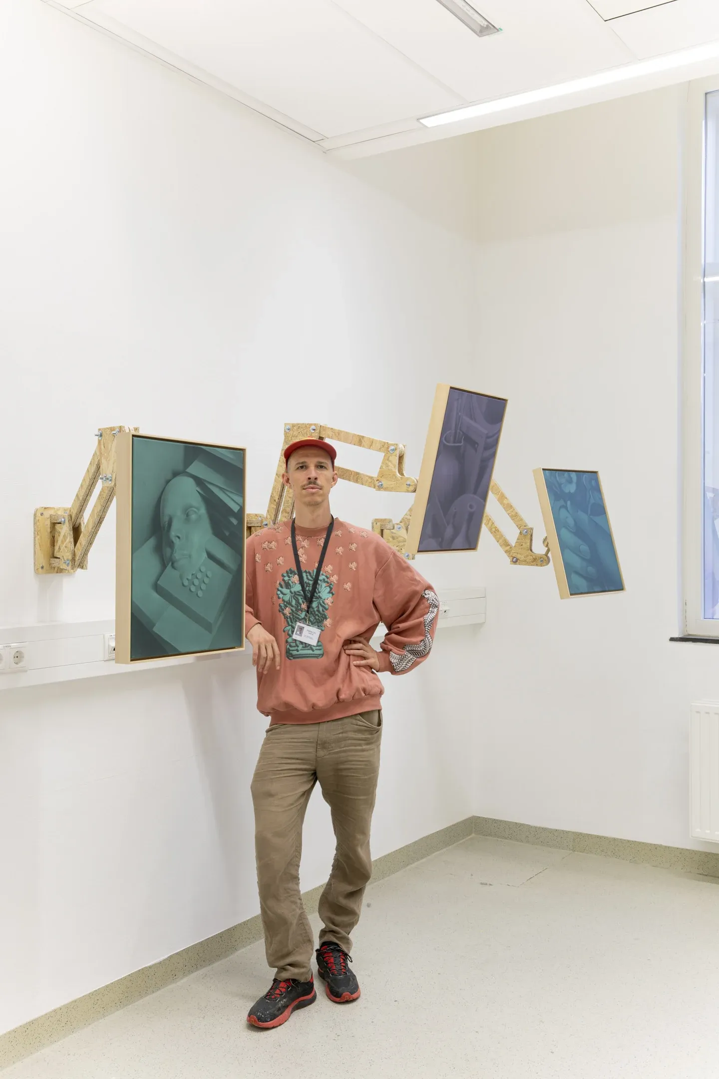 Artist portrait of Paul Riedmüller at Parallel Vienna 2024 standing next to articulated wall-mounted installation with framed images in a gallery setting