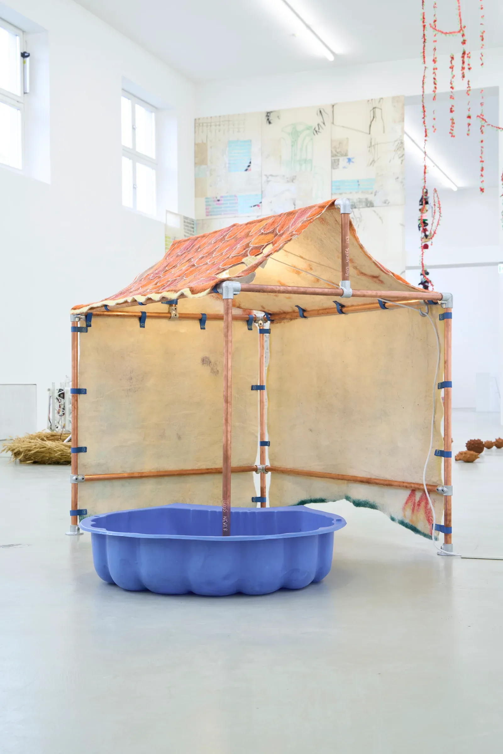Pierre-Yves Delannoy, The Shell Cannot Land on the Playhouse (2025), felt textile house installation with copper pipe structure and small plastic pool, contemporary sculptural environment combining textile, architecture and domestic imagery.