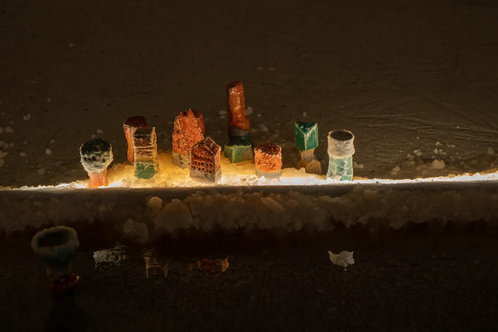 Pierre-Yves Delannoy, I felt your fleece in the tidal valley (2023), installation detail showing small sculptural forms resembling miniature architectures placed along illuminated salt-lined reflective pools in a dark gallery space.