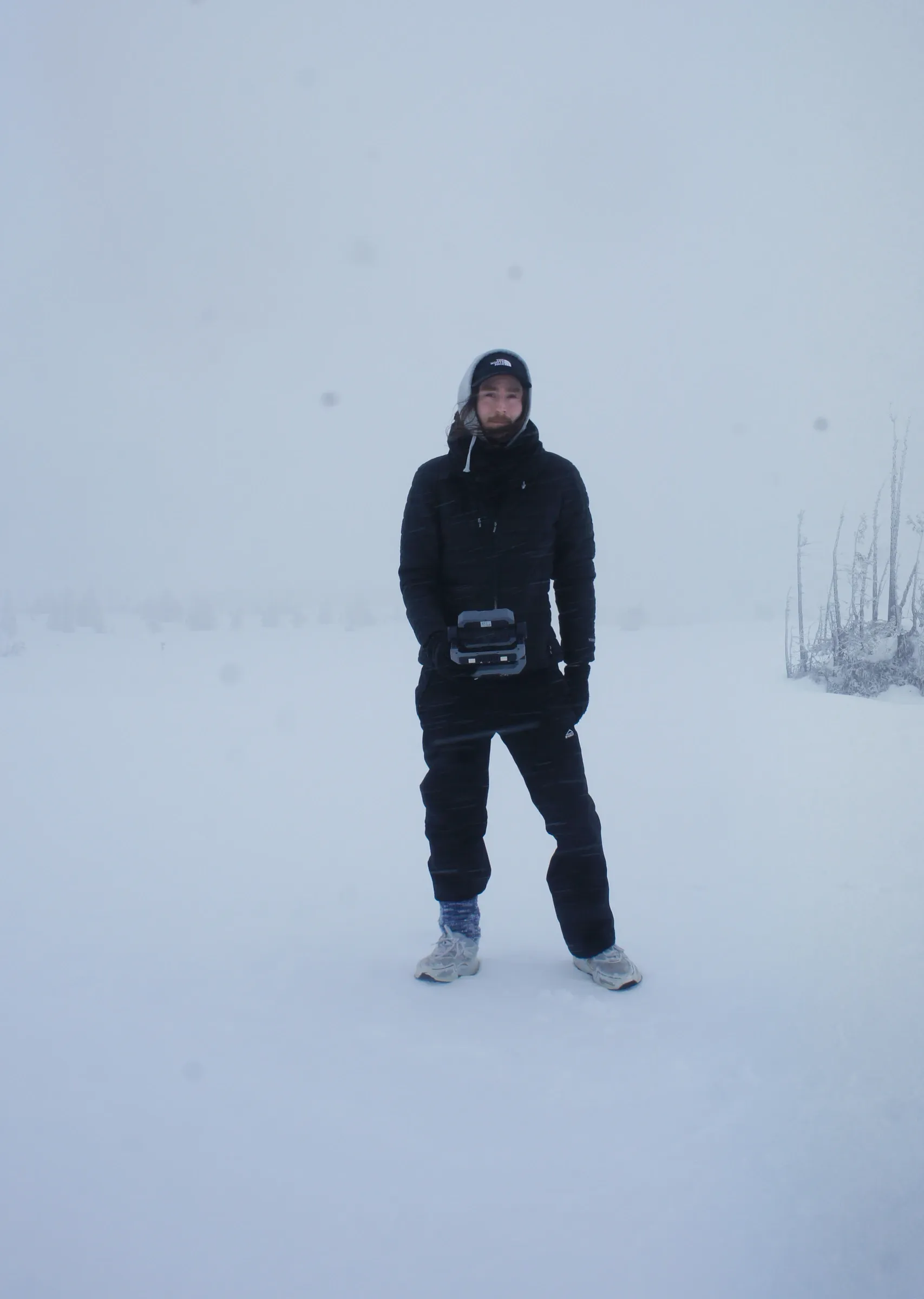 Artist portrait in snowstorm holding camera, Akkanålke 2025, interview with Ernst Koslitsch for Catapult Contemporary Art, Photo Andreas R Andersson