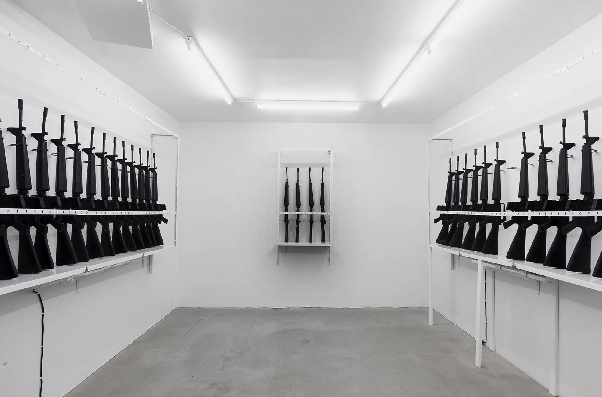 Andreas R Andersson:  Installation with rows of black rifle forms on shelves, The Thousand Yard Stare, Gallery Box Gothenburg 2013–2014, Photo by Martin Hultén