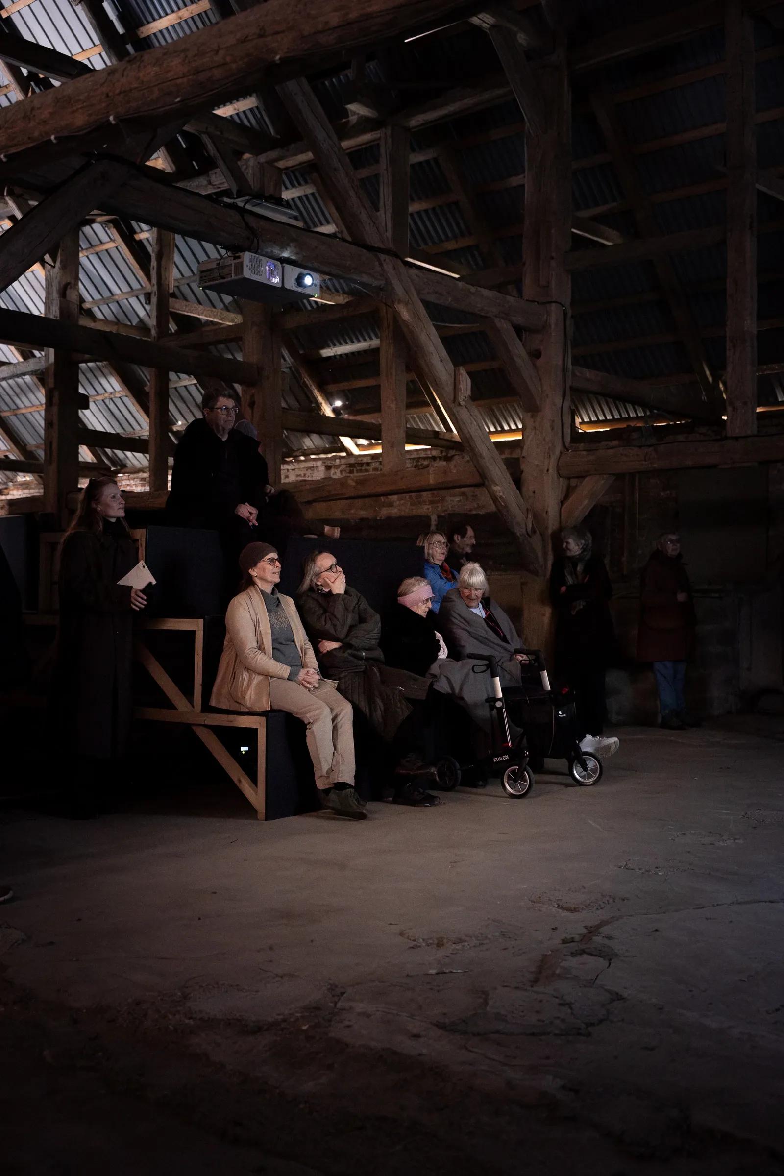 Audience seated inside a wooden barn during the opening of Yalda Afsah’s exhibition Surge at Kunsthal Thy, Denmark, with exposed beams and concrete floor visible.