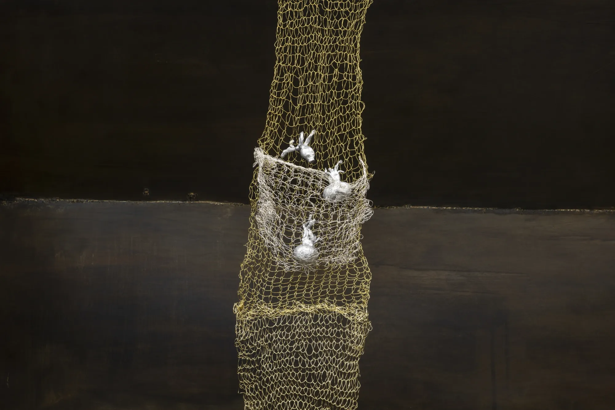 Maija Fox Hard Shoulders detail showing woven metal wire with small cast aluminium plant forms embedded against dark metal surface