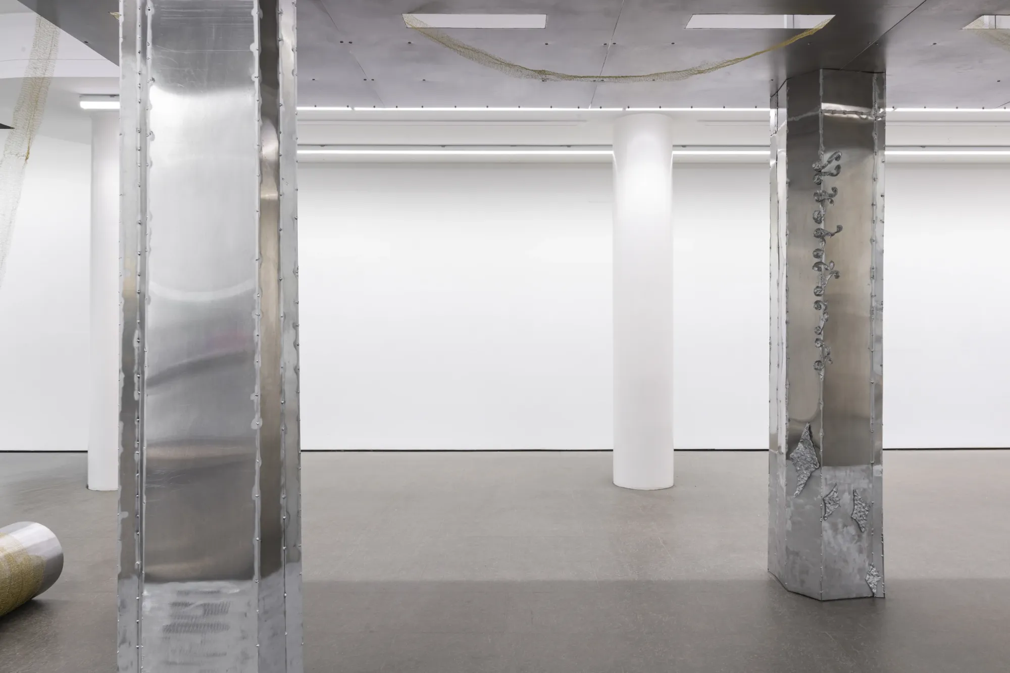 Maija Fox Hard Shoulders installation view showing metal columns with cast aluminium details and hanging woven wire elements framing steel object in gallery