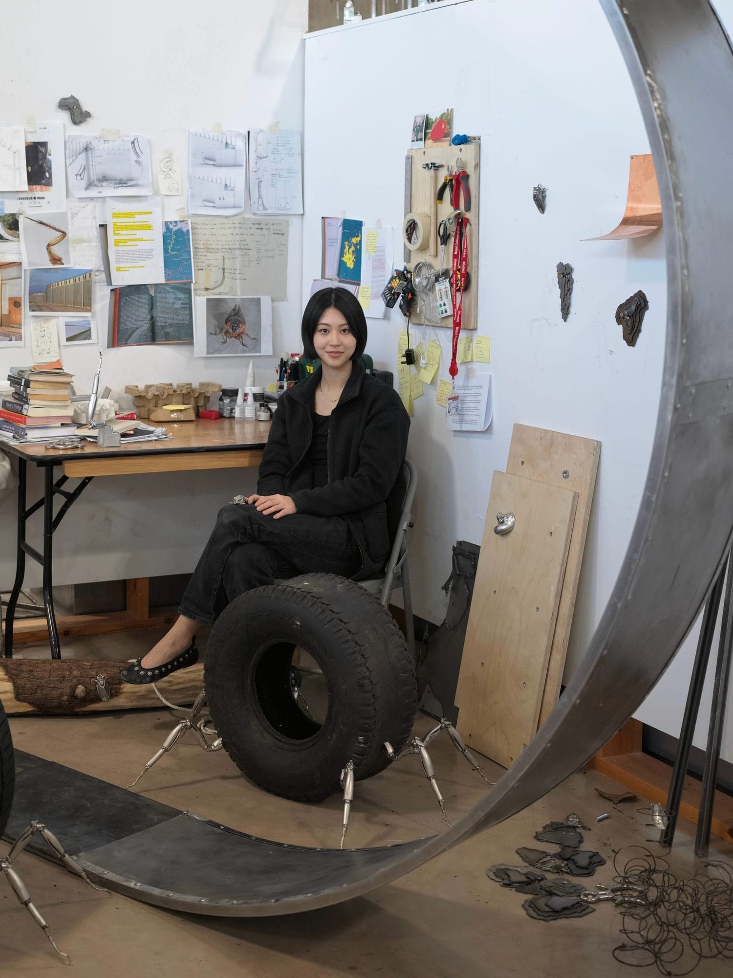 Shirley Fu portrait in studio London seated beside tyre sculpture with metal structure tools and materials on floor photo by Zhongting Sun