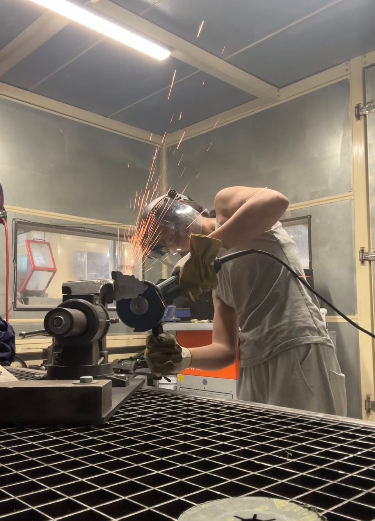 Shirley Fu working in studio grinding metal with sparks wearing protective mask and gloves during fabrication process