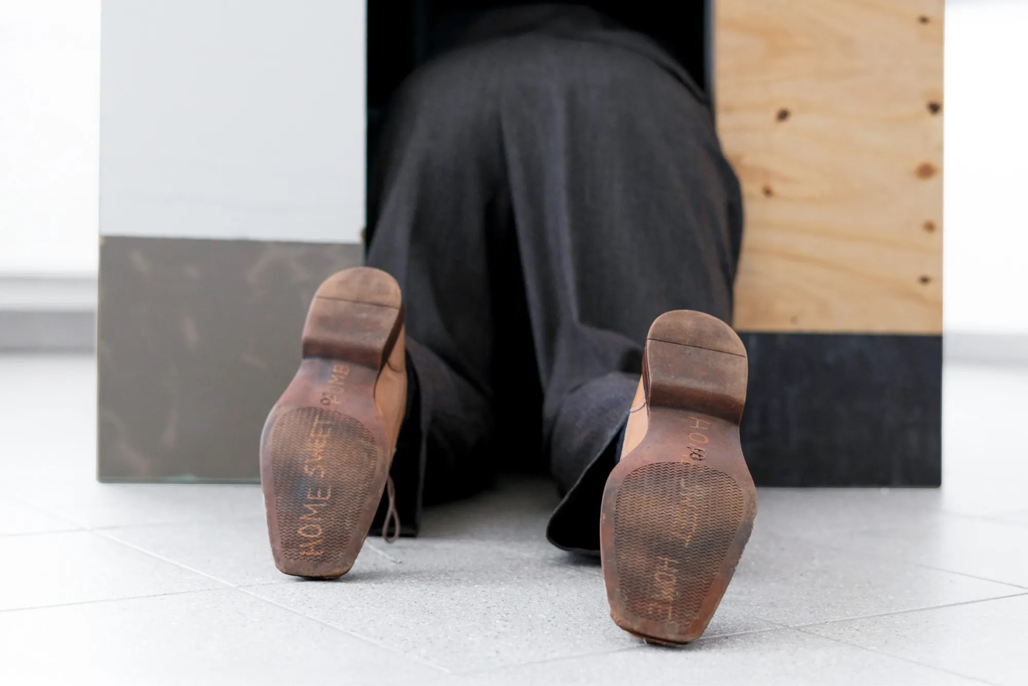 Stasia Grishina Man on all fours detail legs and shoes entering wooden doghouse sculpture Frankfurt based artist installation
