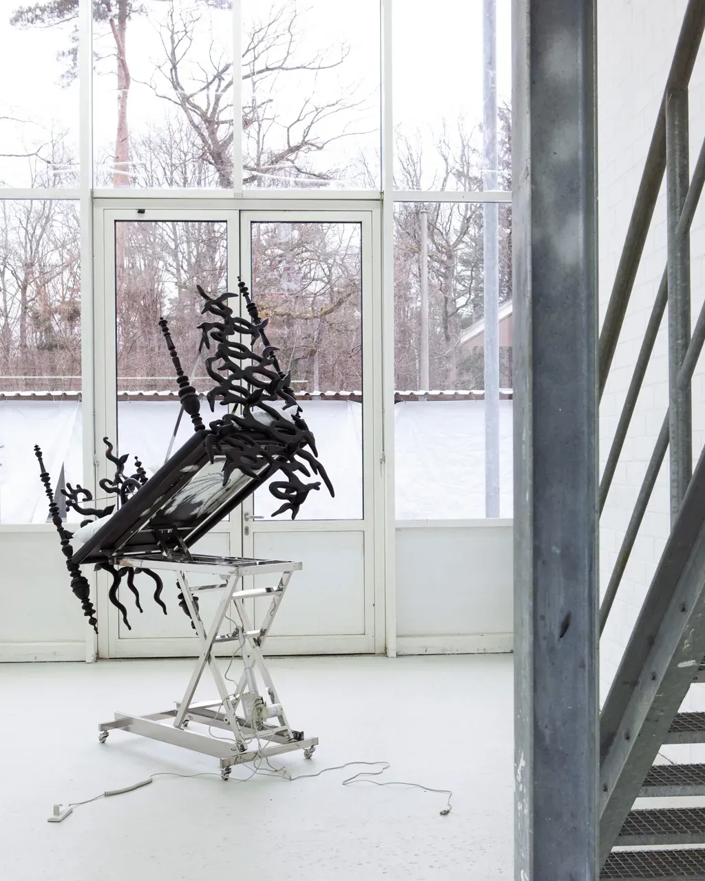 Vivienne Sun Liminality installation with reclining medical chair overgrown with black organic sculptural forms in bright institutional space