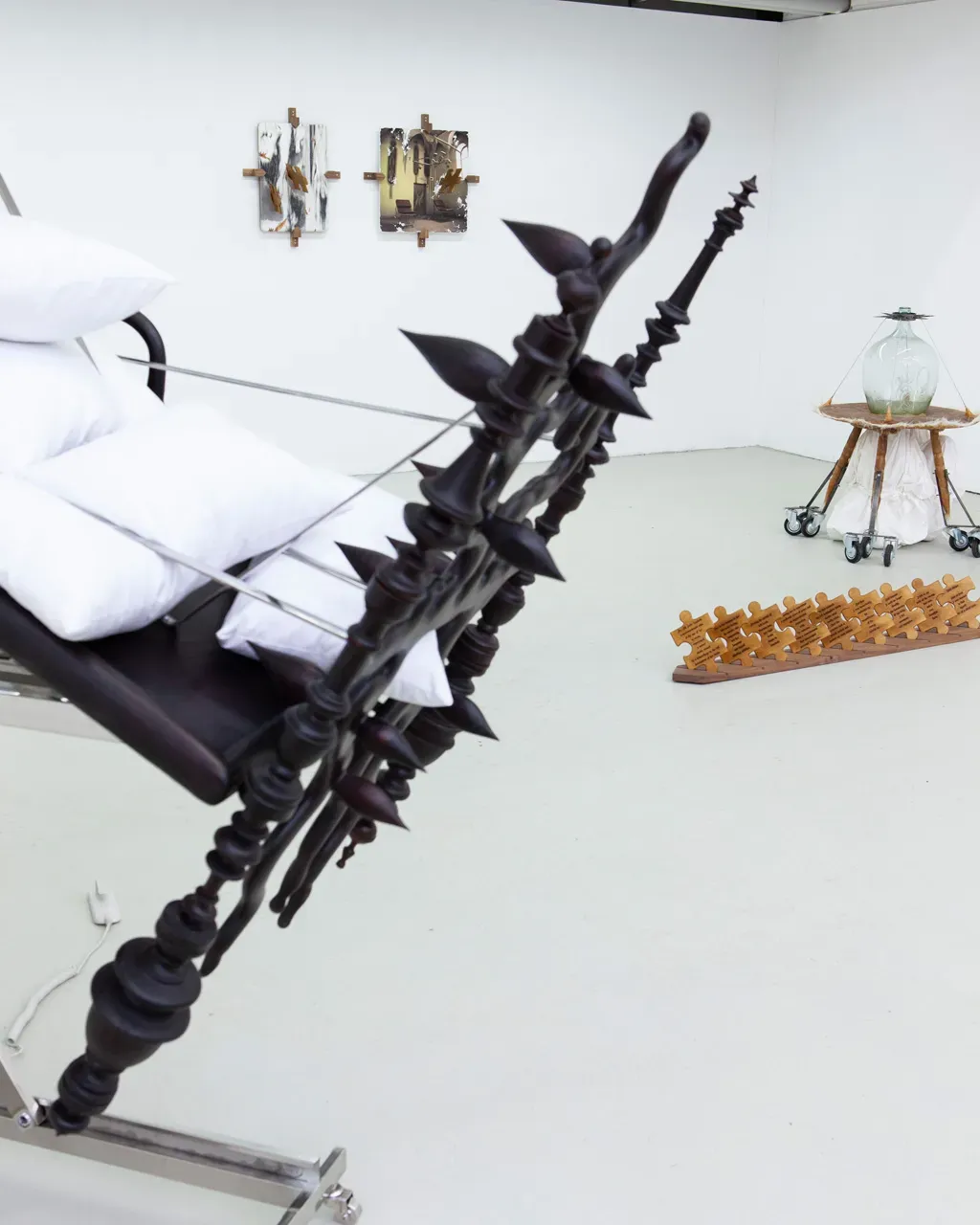 Vivienne Sun Liminality installation with reclining chair, puzzle-shaped wall works, and glass vessel on wheeled cart in gallery space