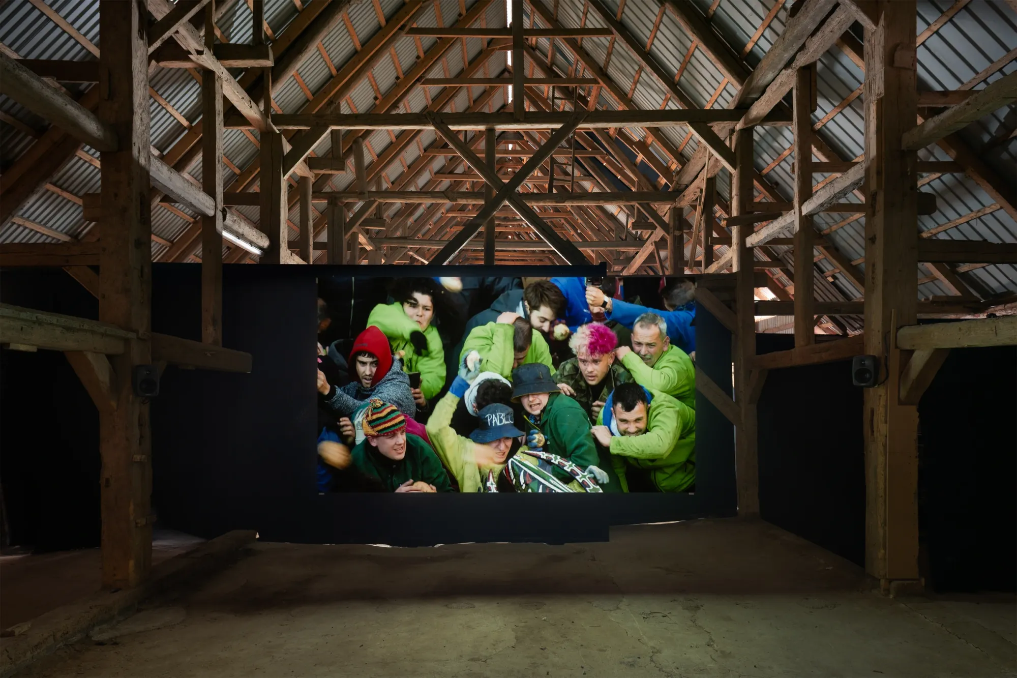 Installation view of Yalda Afsah’s exhibition Surge at Kunsthal Thy, Denmark, showing a large video projection of a dense crowd in motion inside a wooden barn with exposed beams and concrete floor.
